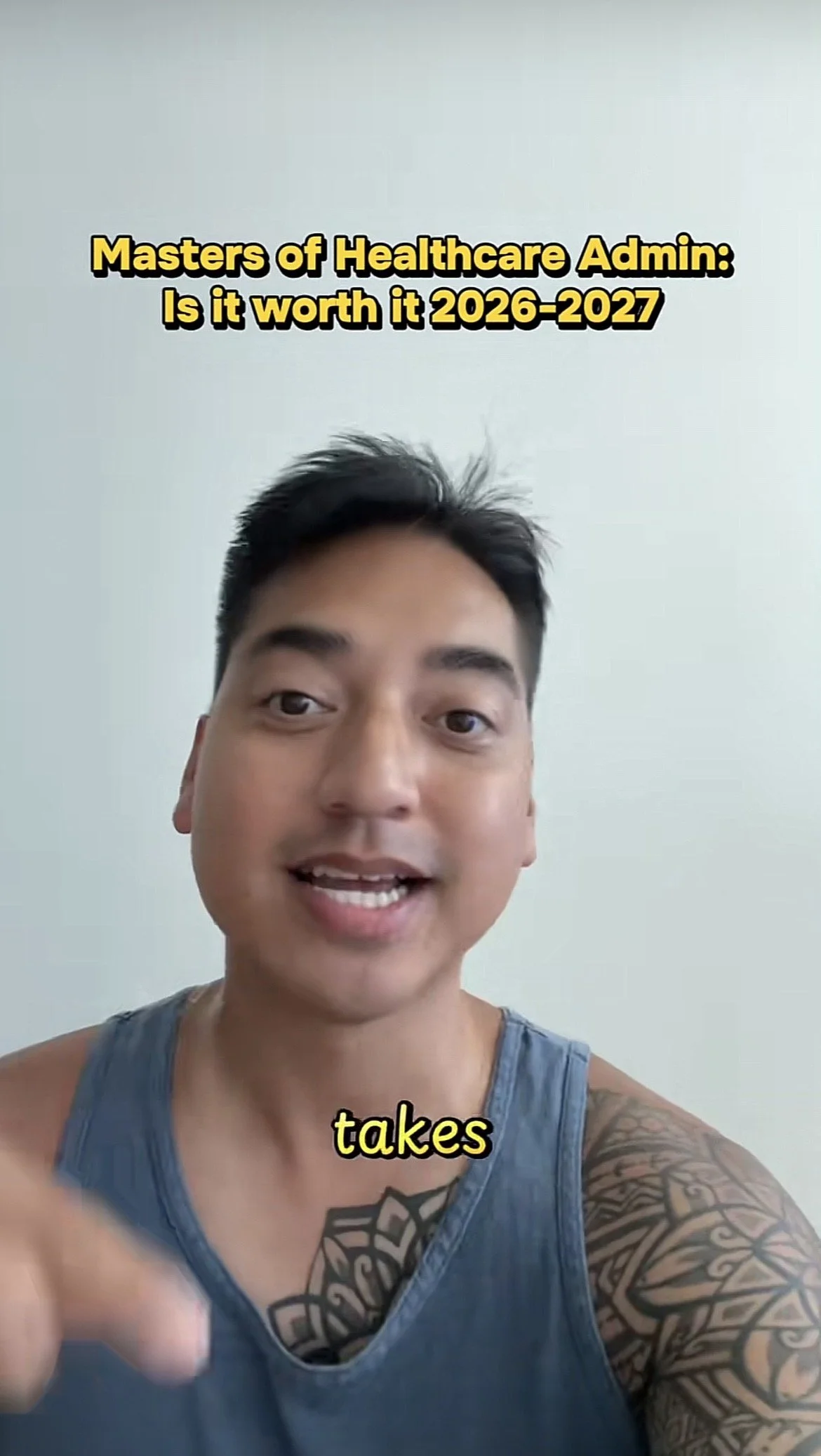 A young man with tattoos on his arms and a tattoo on his chest, wearing a gray tank top, speaking directly at the camera with a plain white wall in the background. Text above his head reads, 'Masters of Healthcare Admin: Is it worth it 2026-2027,' and partially visible text below says, 'takes.'