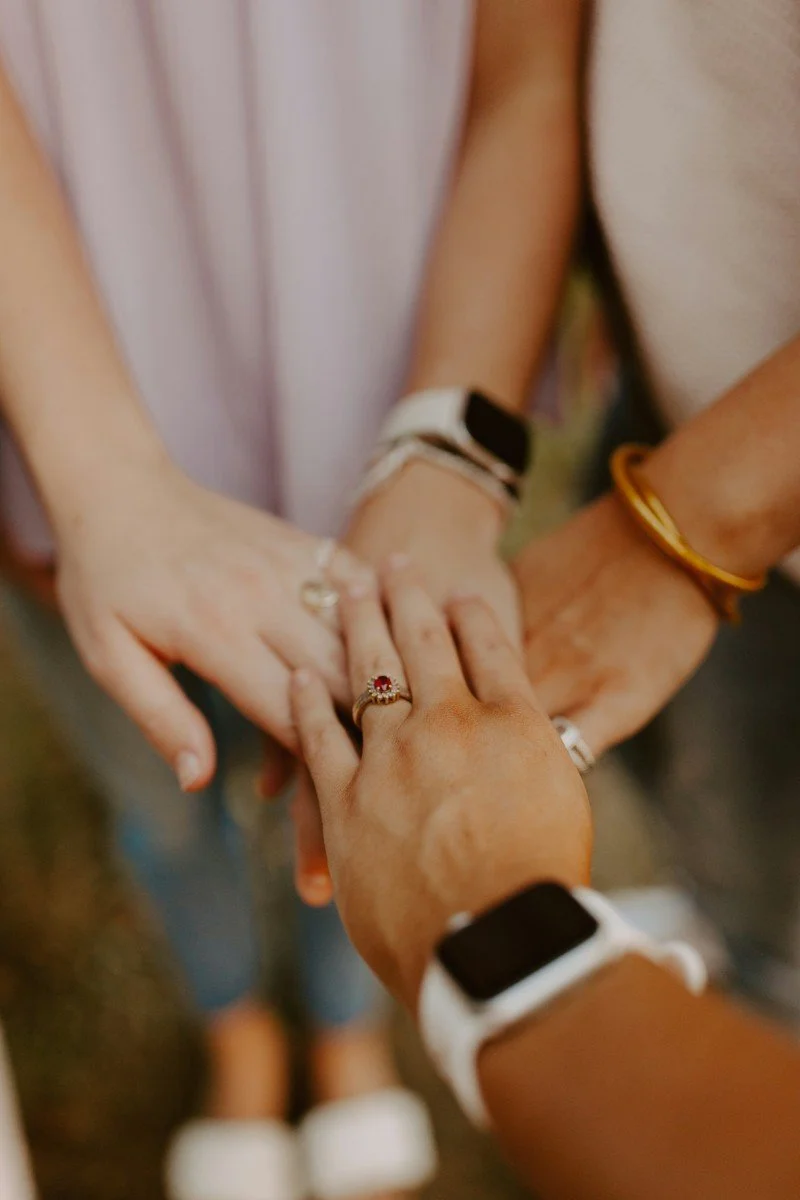 Close-up of four hands stacked together, showing rings and bracelets, symbolizing unity and friendship.