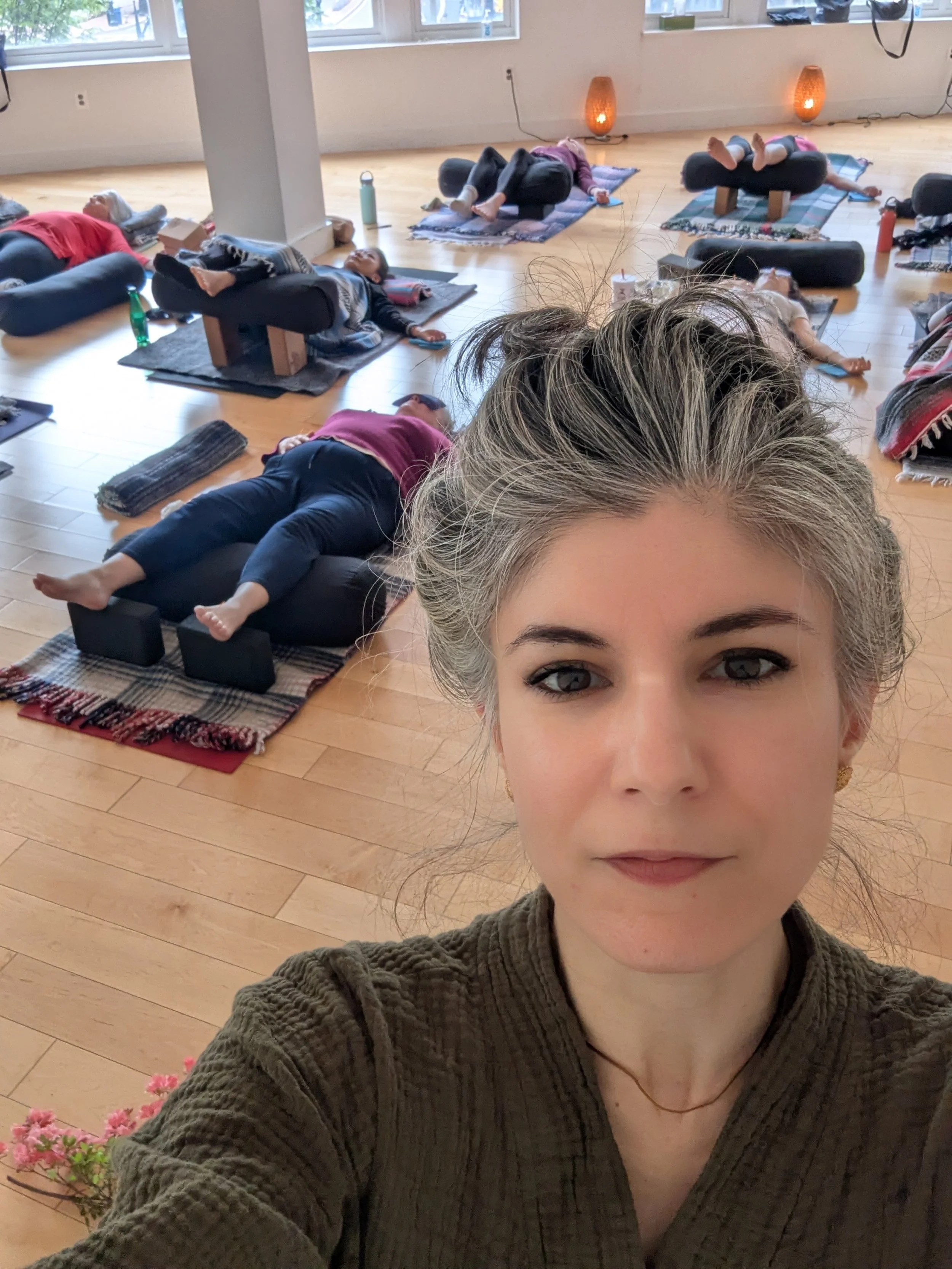 Selfie of the acupuncturist at a workshop, with participants resting on yoga mats behind her