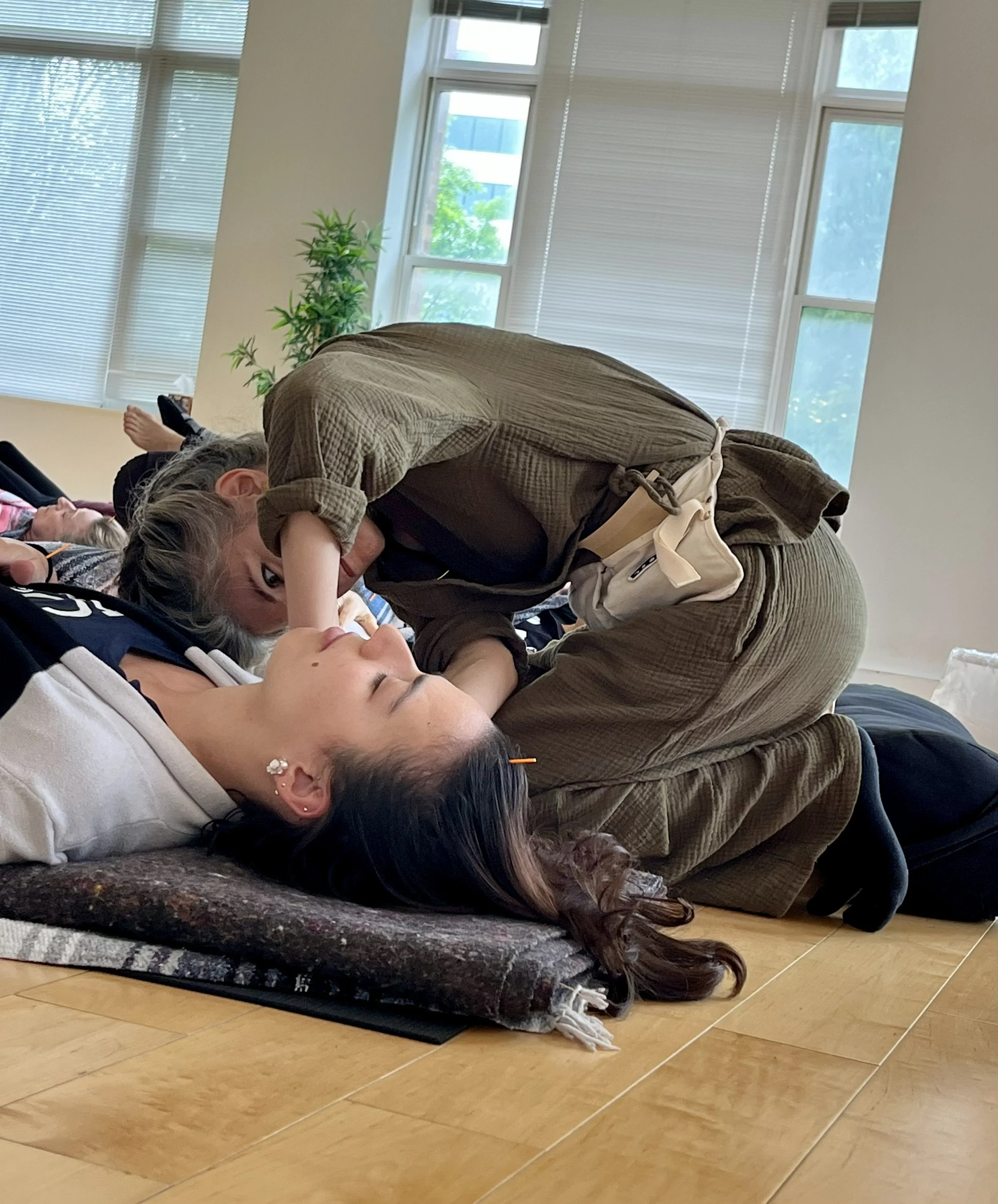 An acupuncturist kneels to place needles for a participant lying on a mat at a group workshop