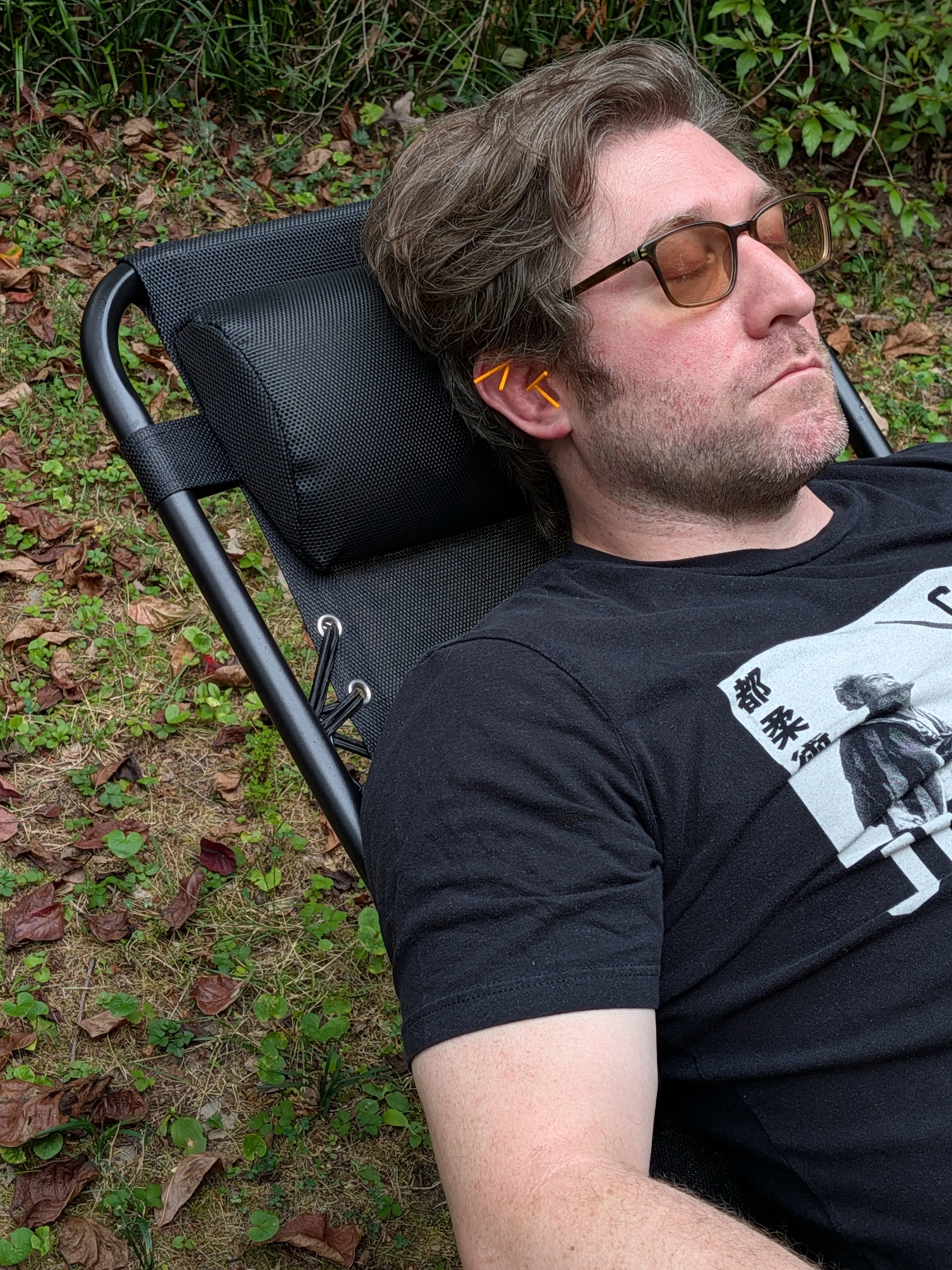 A man relaxes in a zero-gravity chair outdoors with ear acupuncture needles in place
