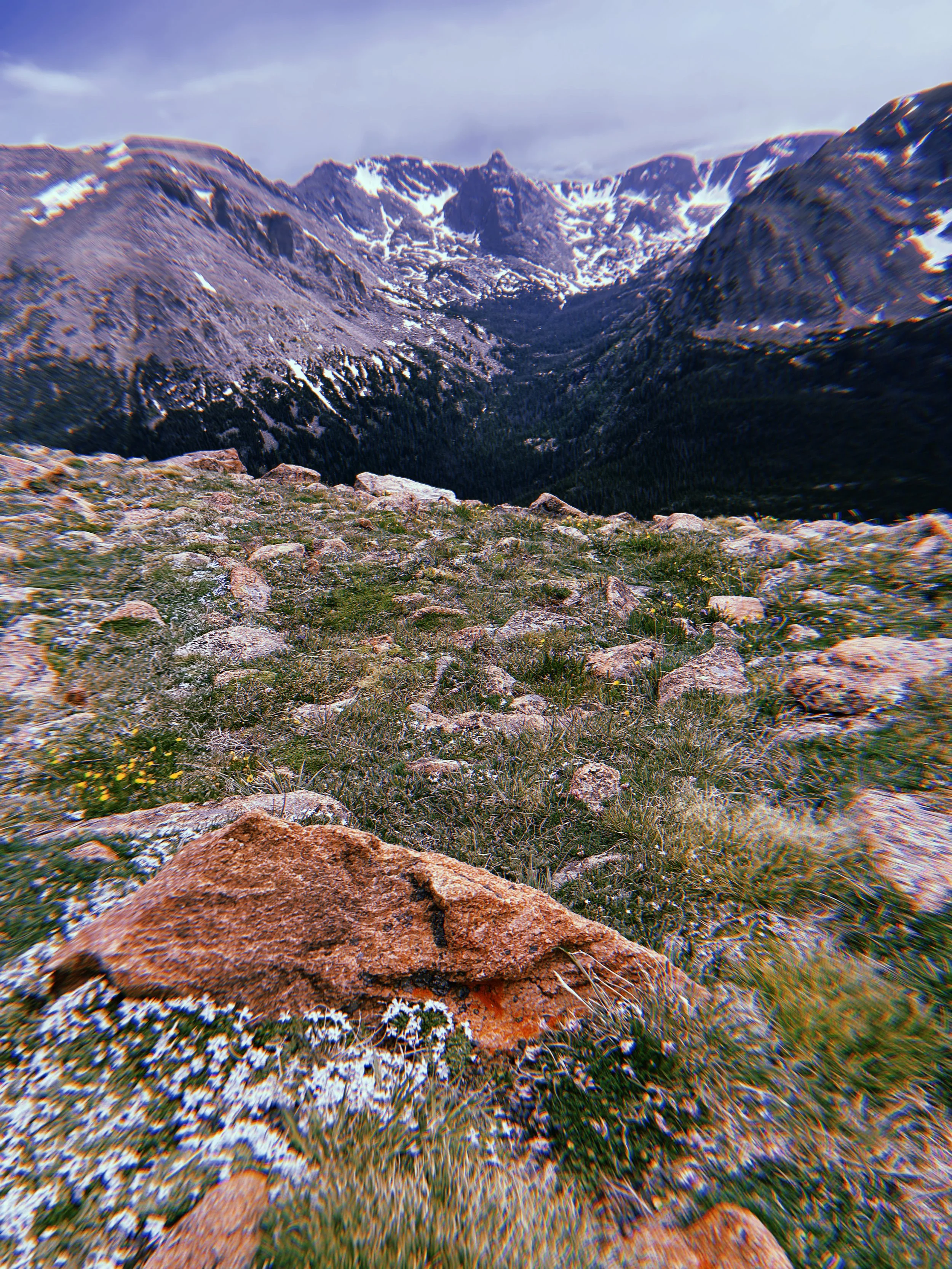 Snow-capped mountains with rocky foreground and a cloudy sky.
