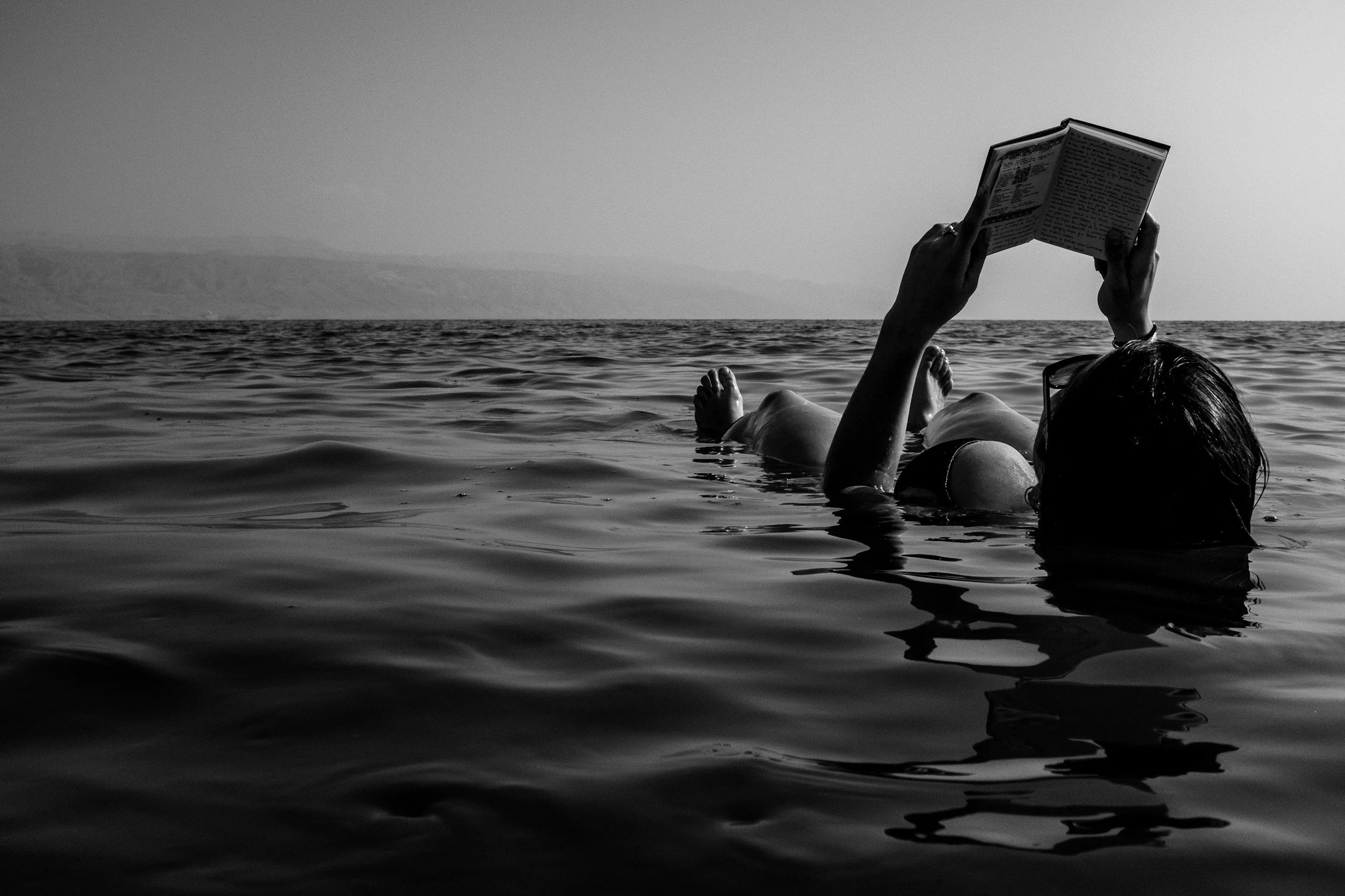woman floating in ocean reading a book while her website is built for her