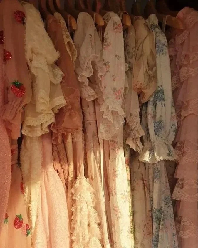 Vários vestidos de encantamento e renda com detalhes em cor de rosa e floral, pendurados em cabides.