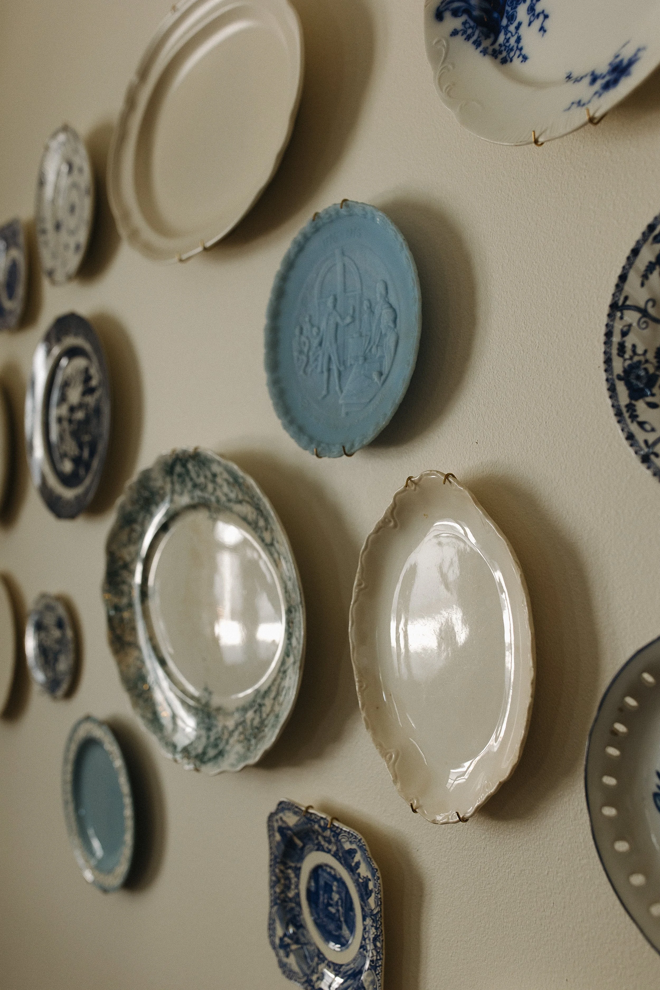 Collection of decorative ceramic plates and bowls arranged on a wall, with some plates featuring blue and white patterns and others with embossed designs.