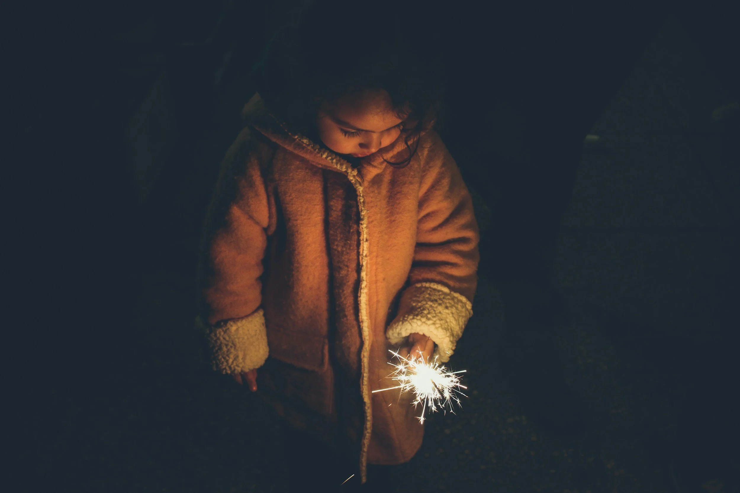 A young girl in a warm coat holding a sparkler at night.