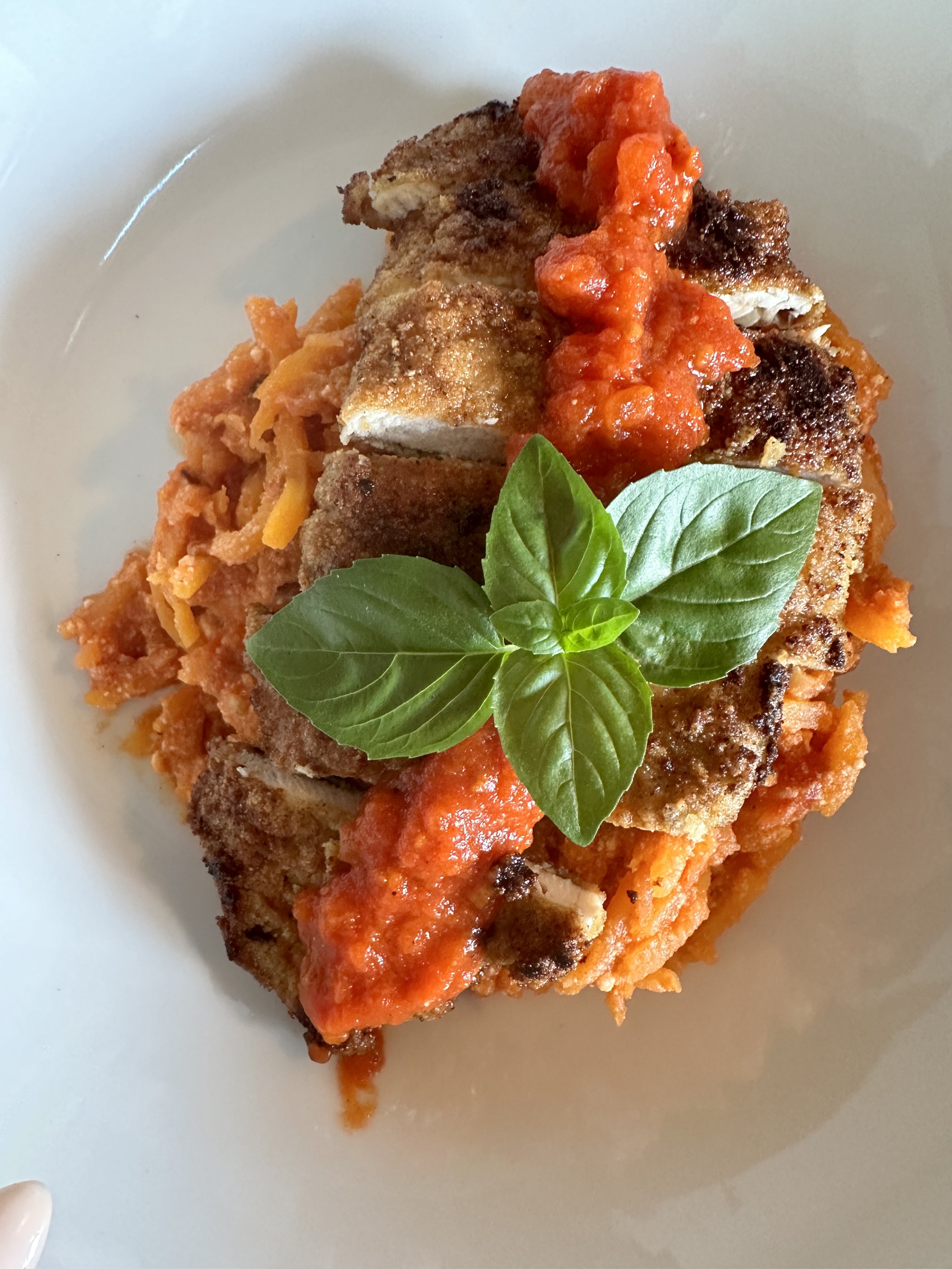 Breaded fried fish fillet topped with red tomato sauce, served with shredded vegetables and fresh basil leaves.