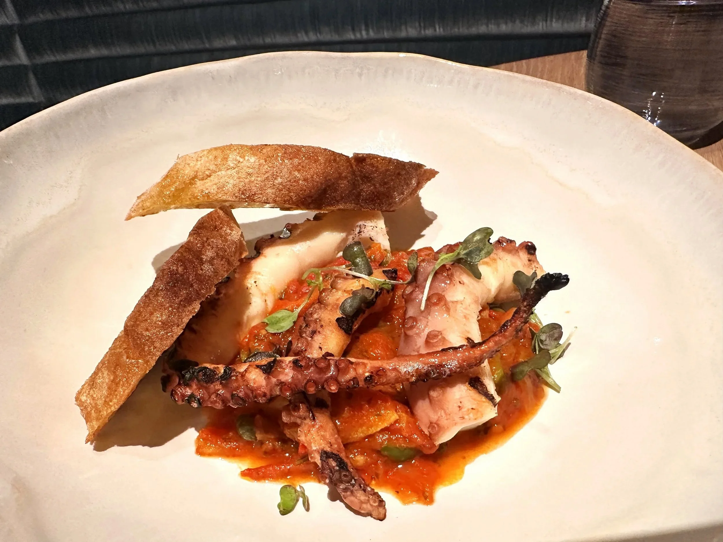 A plate of grilled seafood topped with fresh herbs, accompanied by two slices of toasted bread.