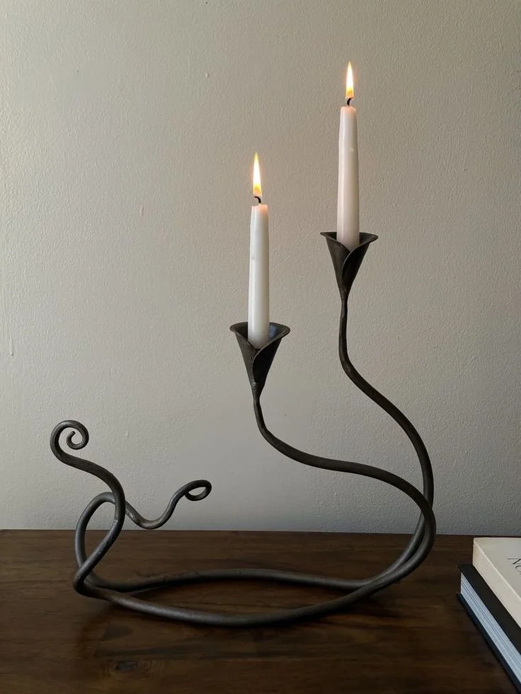 A decorative metal candle holder with two lit white candles on a wooden surface against a plain wall.