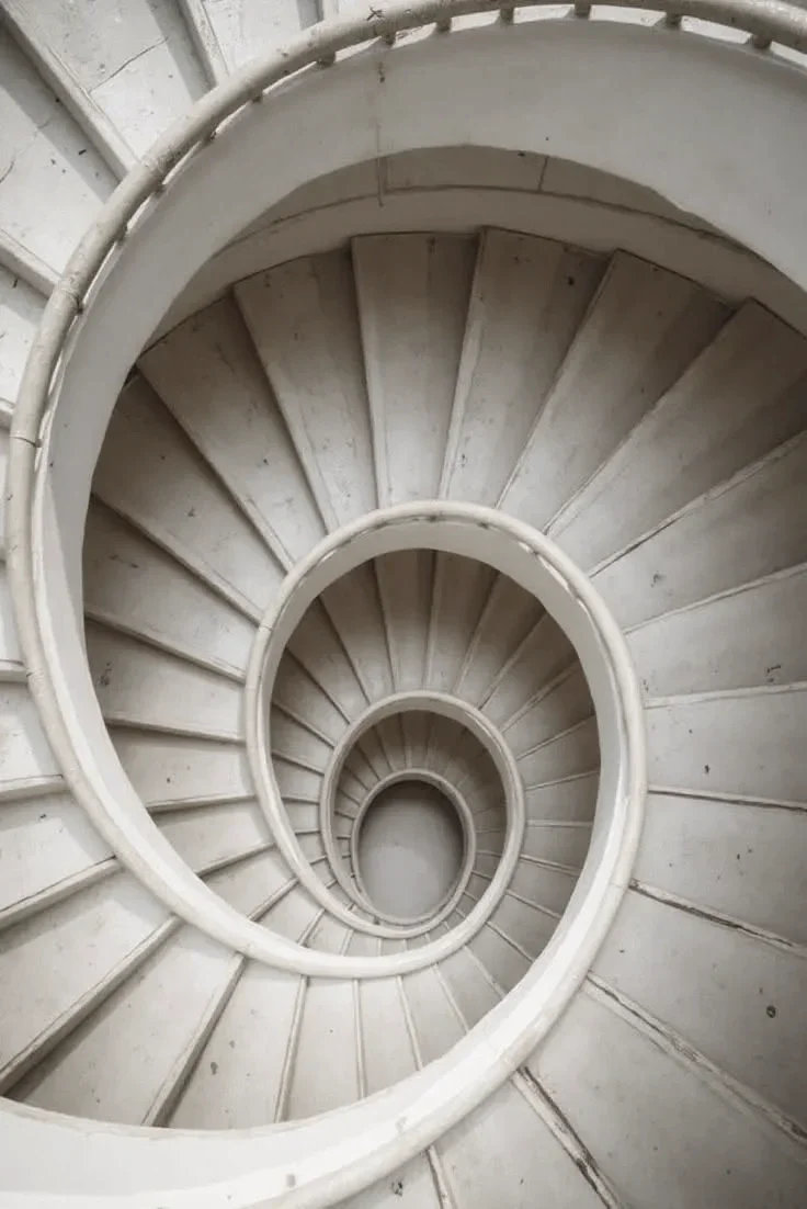 A view looking down a spiral staircase with white railings and steps, creating a circular pattern.