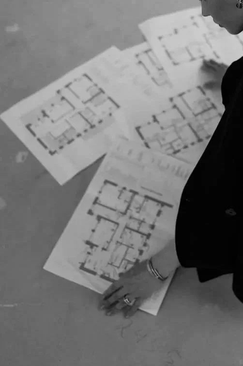 Person examining architectural blueprints or floor plans on a table.