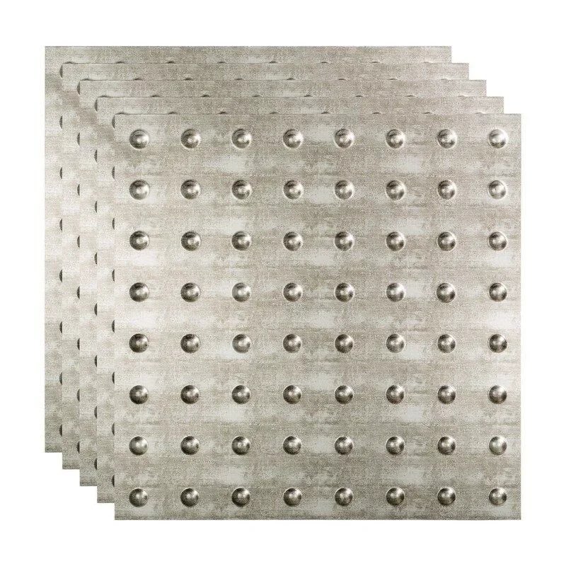 Four stacked metal sheets with evenly spaced raised circular bumps on a concrete or metallic surface.