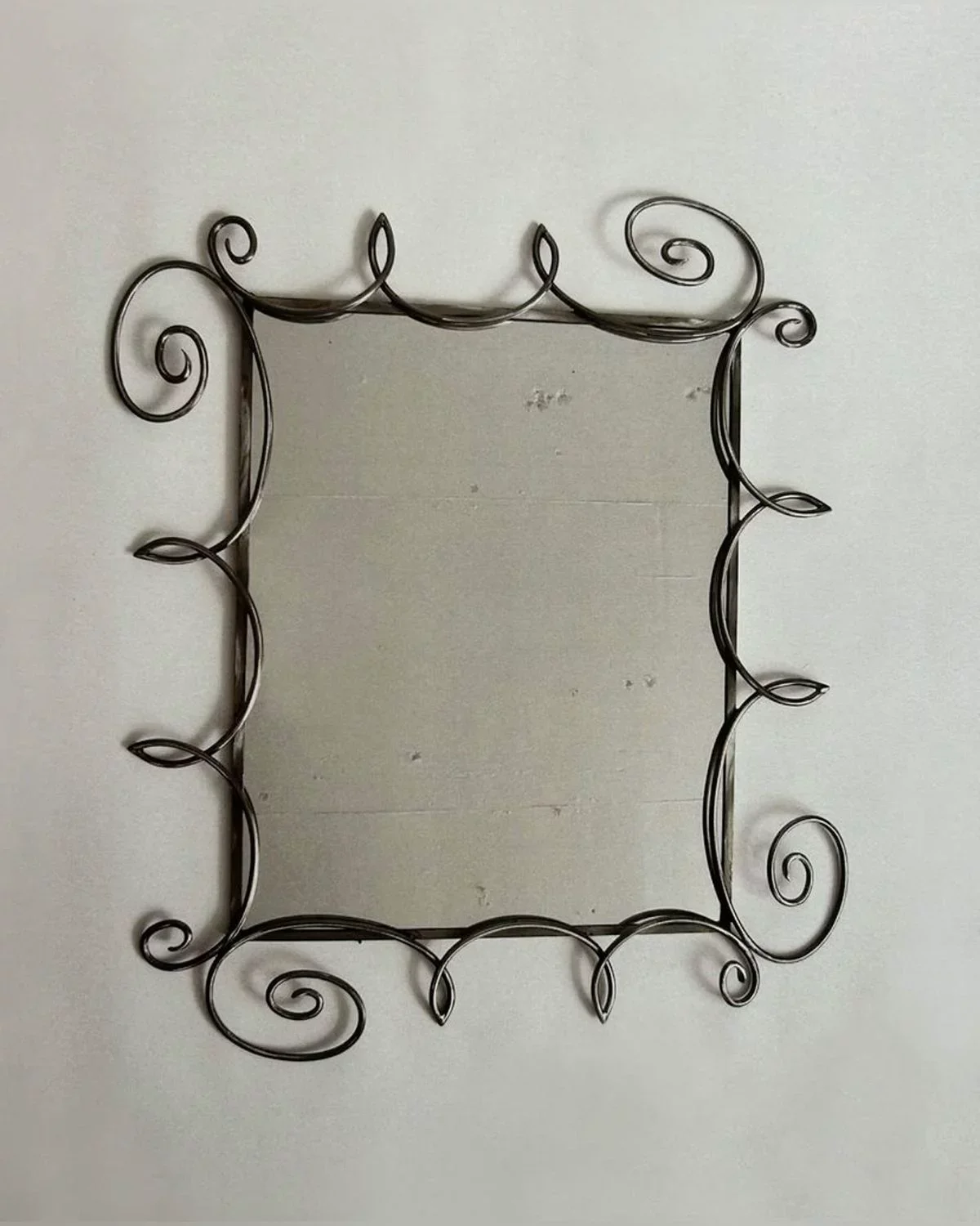 Decorative black metal photo frame with ornate, swirling designs around the edges, hung on a plain wall.