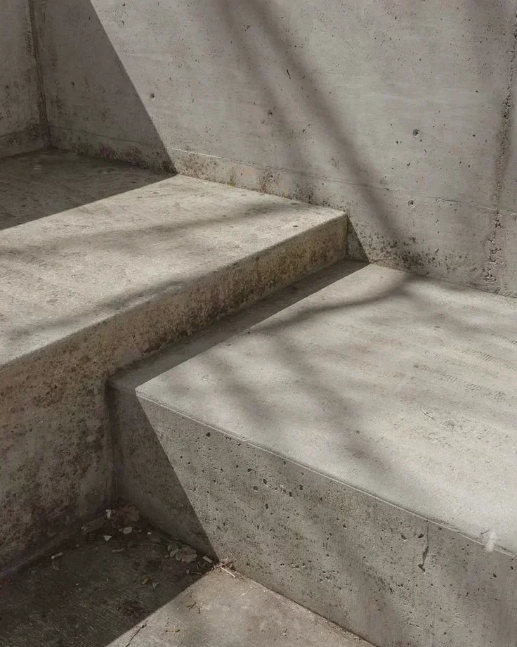 Concrete stairs and floor with shadows cast by a nearby object or plant.