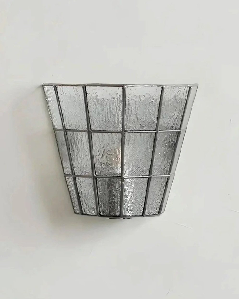 A metal wall sconce with a textured, frosted glass cover mounted on a plain white wall.