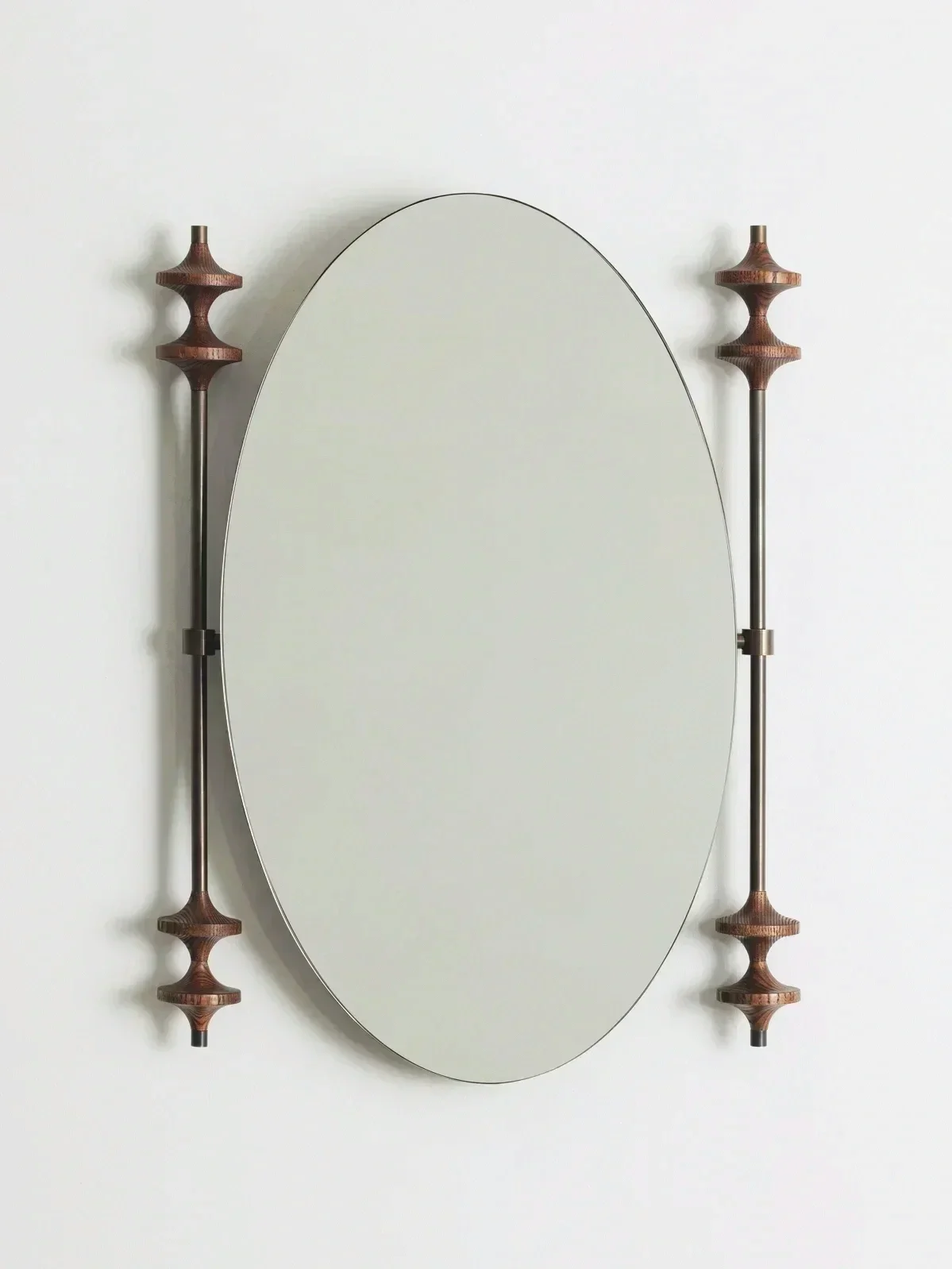 An oval mirror mounted on a white wall with dark wooden decorative posts on each side.