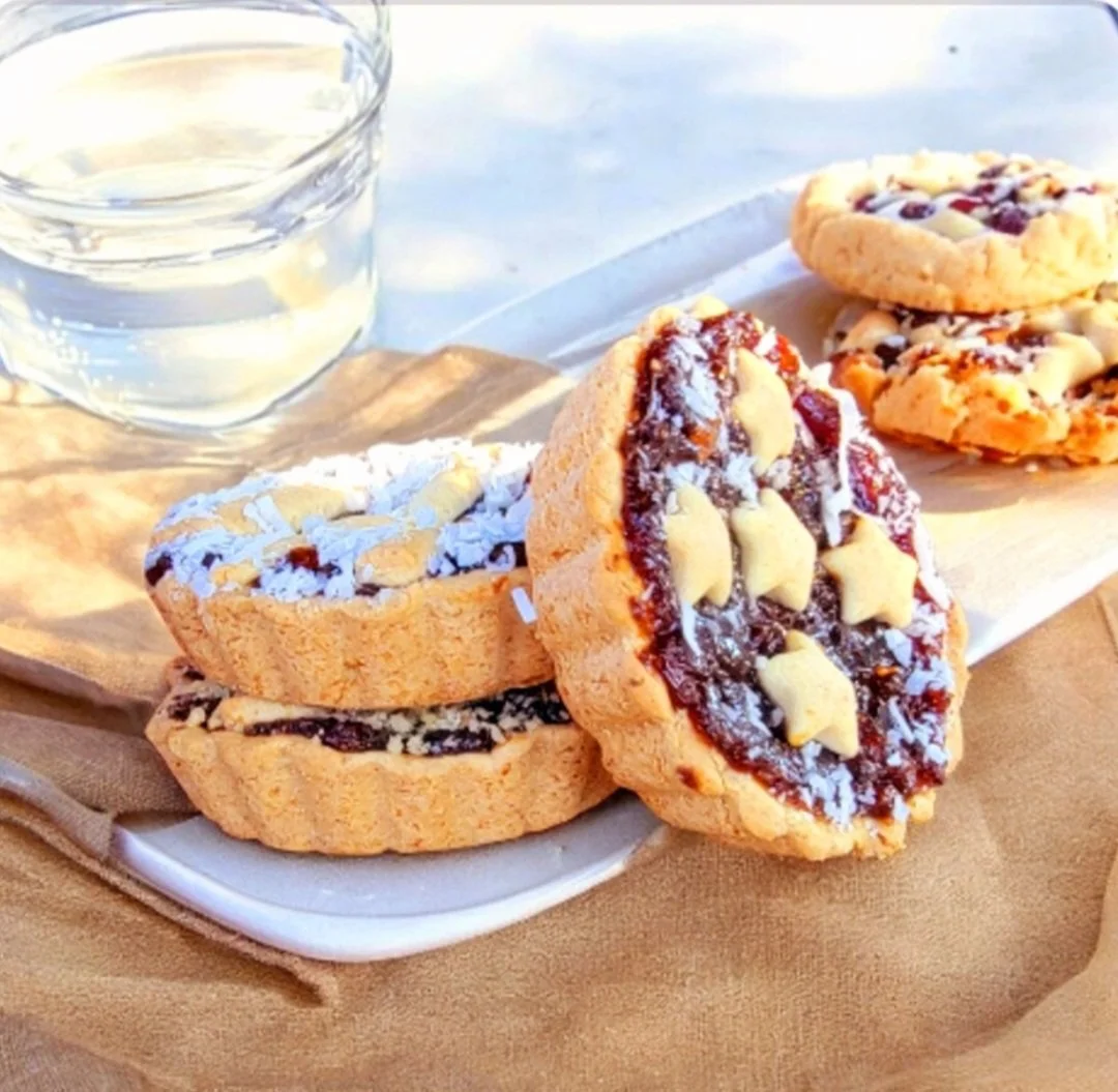 Close-up of three decorated cookies on a white serving dish with a glass of water nearby, on a beige cloth surface.