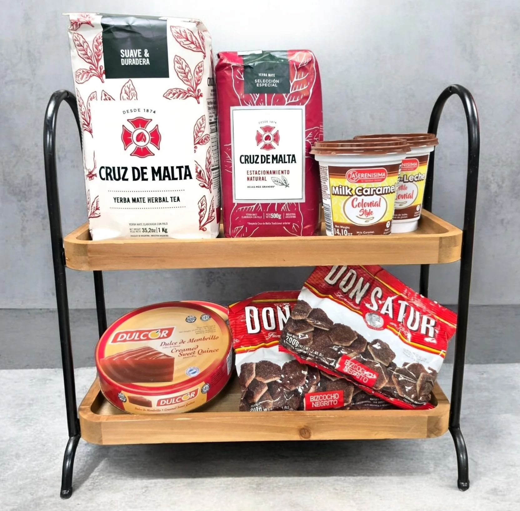 A two-tier wooden and metal cart holding various food products, including packages of yerba mate tea, caramel-flavored milk, and packs of dried beef jerky.