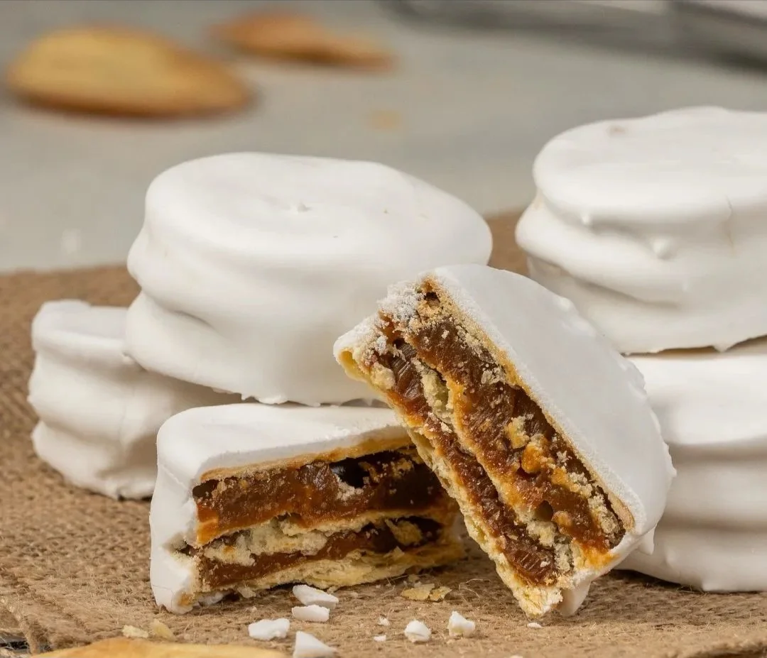 A close-up of several cookies with white icing and a partially broken cookie revealing caramel and chocolate filling.
