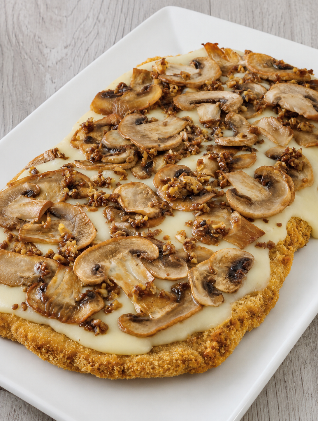 Mushroom and ground meat topping on a breaded, baked dish served on a white rectangular plate