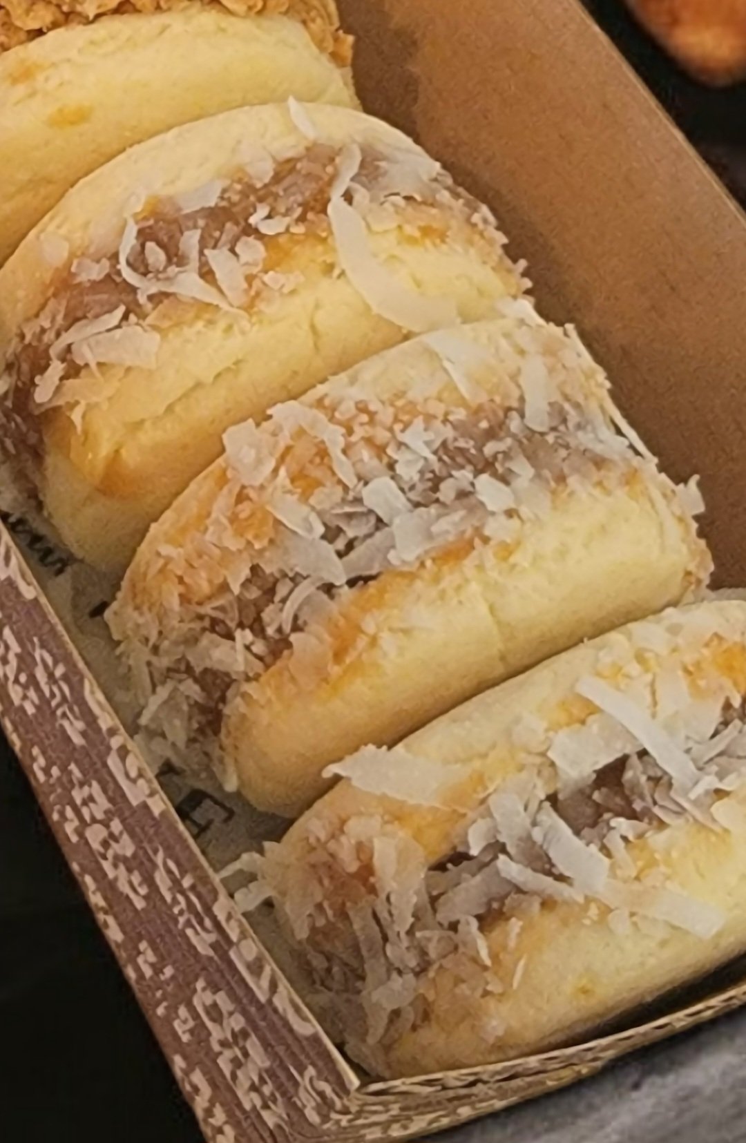 Four yellow cake rolls topped with shredded coconut in a cardboard box.