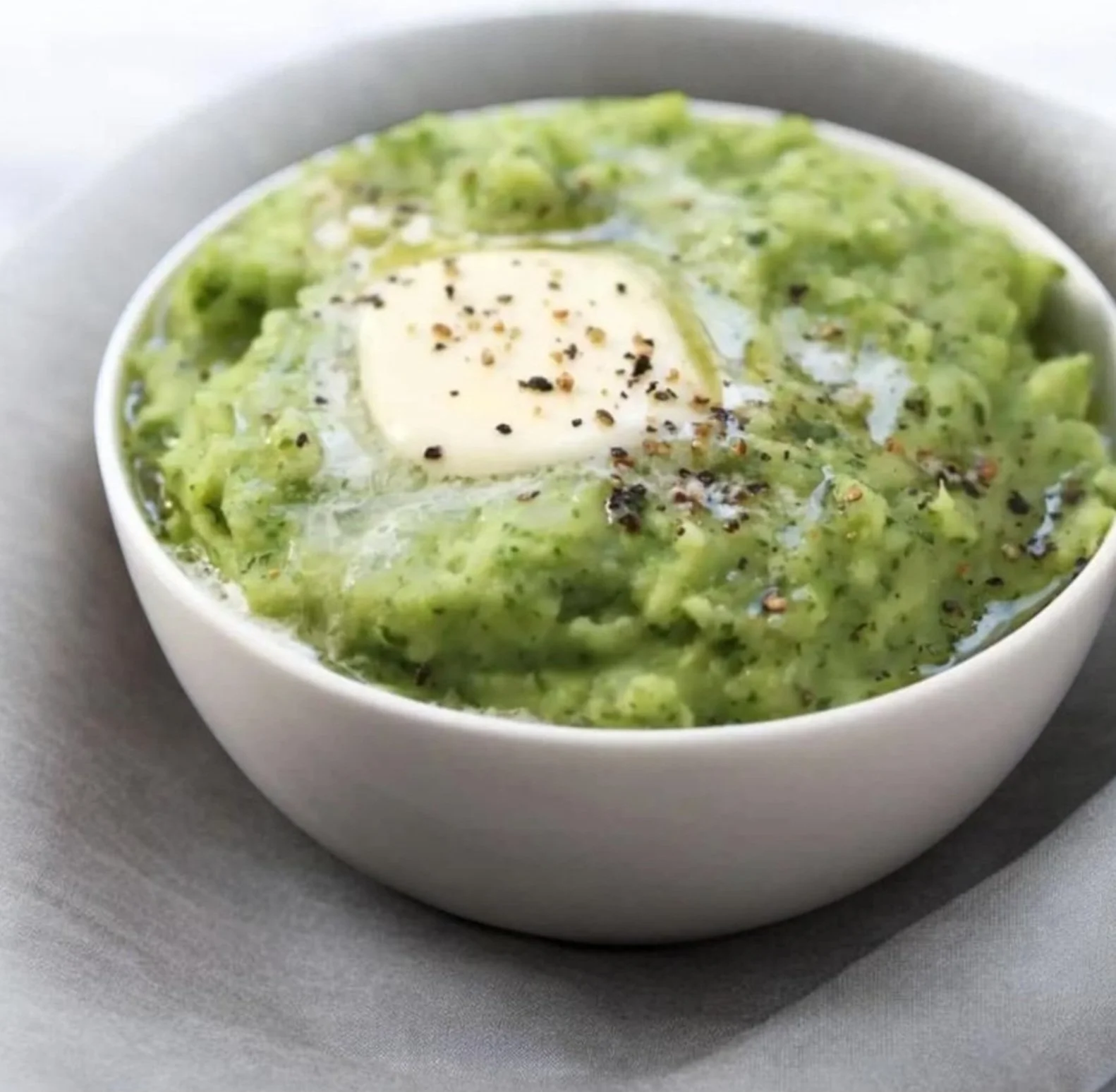 A bowl of creamy green soup topped with black pepper and a dollop of sour cream.