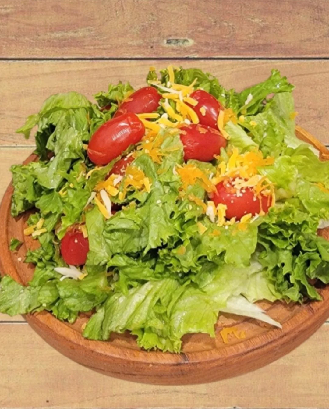 Fresh vegetable salad with lettuce, cherry tomatoes, shredded cheese, on a wooden plate.