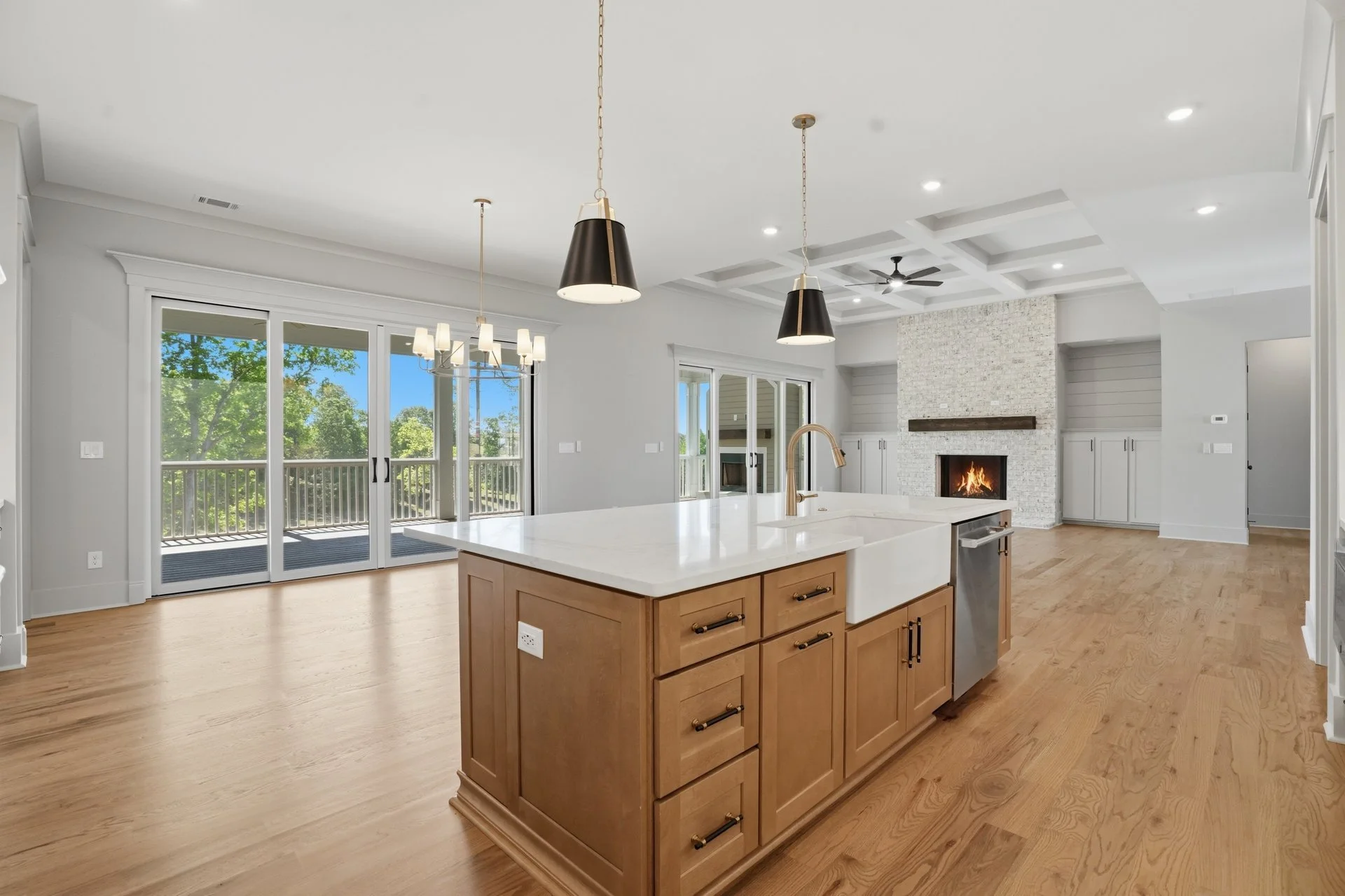 Open-concept living space with kitchen island, pendant lighting, large glass sliding doors, hardwood flooring, fireplace, and built-in cabinets.
