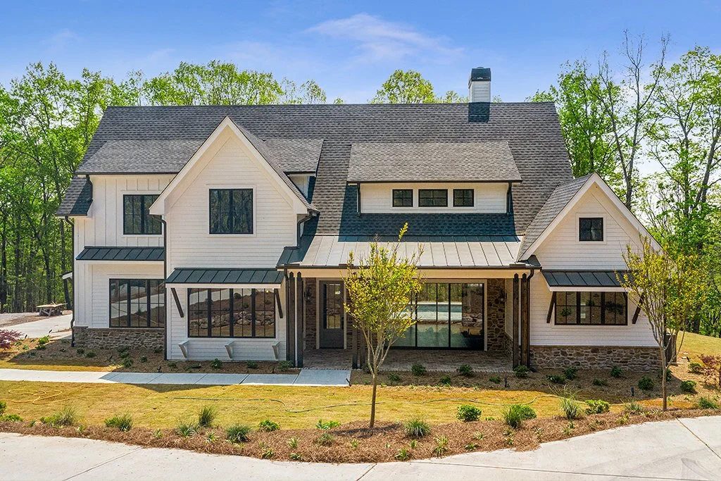 Modern house with white siding, black window frames, and a stone foundation, set in a landscaped yard with small trees and a walkway.