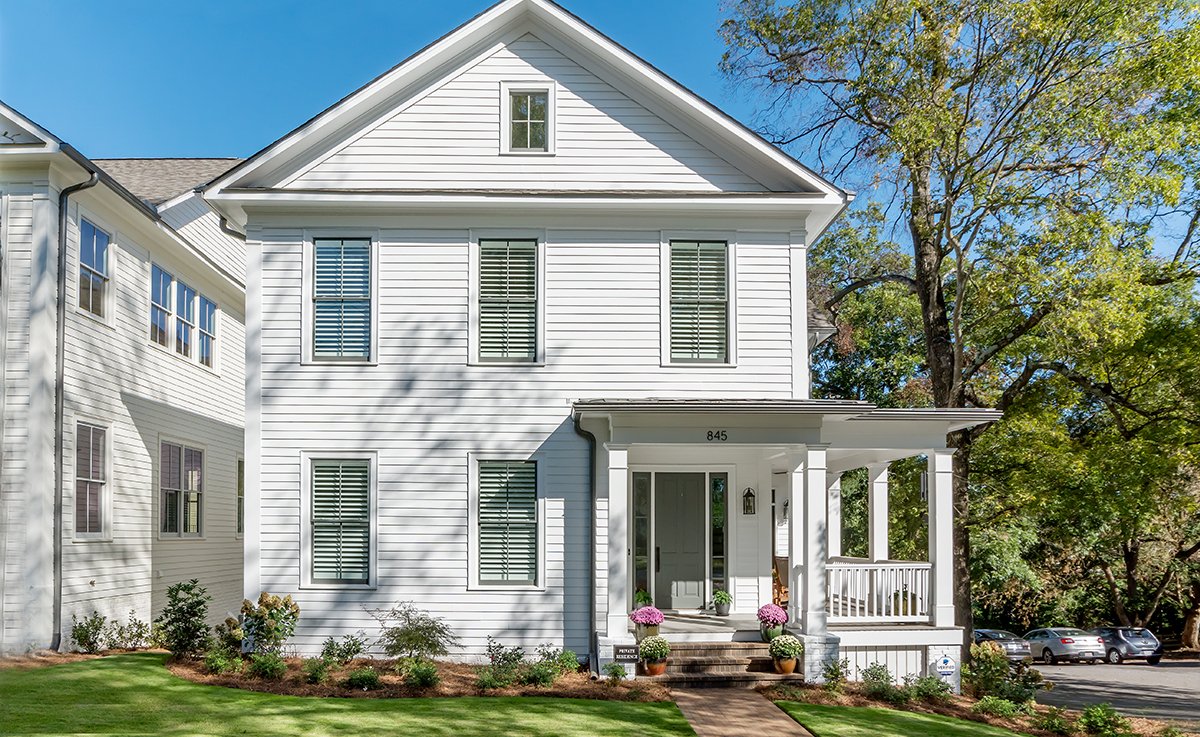 White two-story house with a porch, surrounded by green lawn and trees, during daytime.