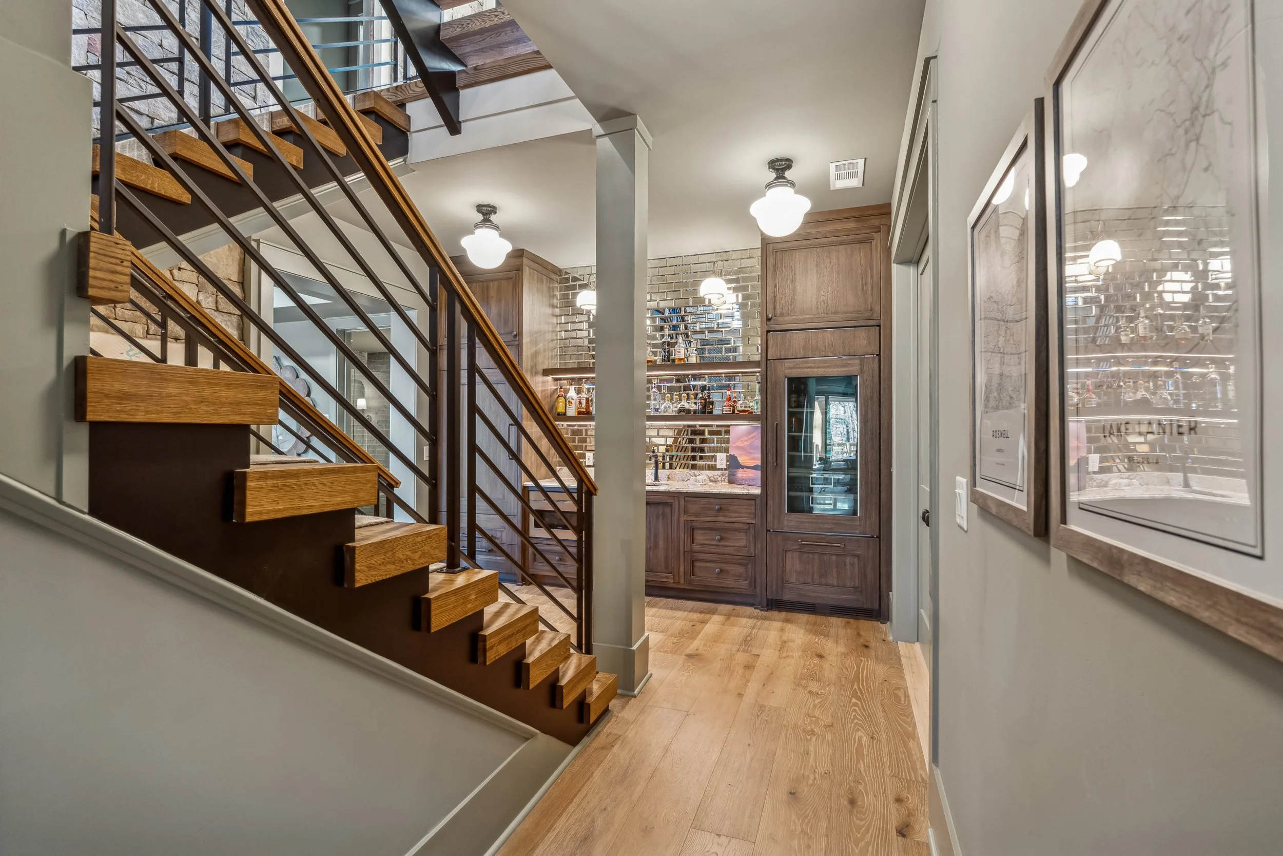 Interior view of a home featuring a staircase with wooden steps and metal railing, a wooden cabinet with glass doors, brick walls, and framed artwork on the wall.
