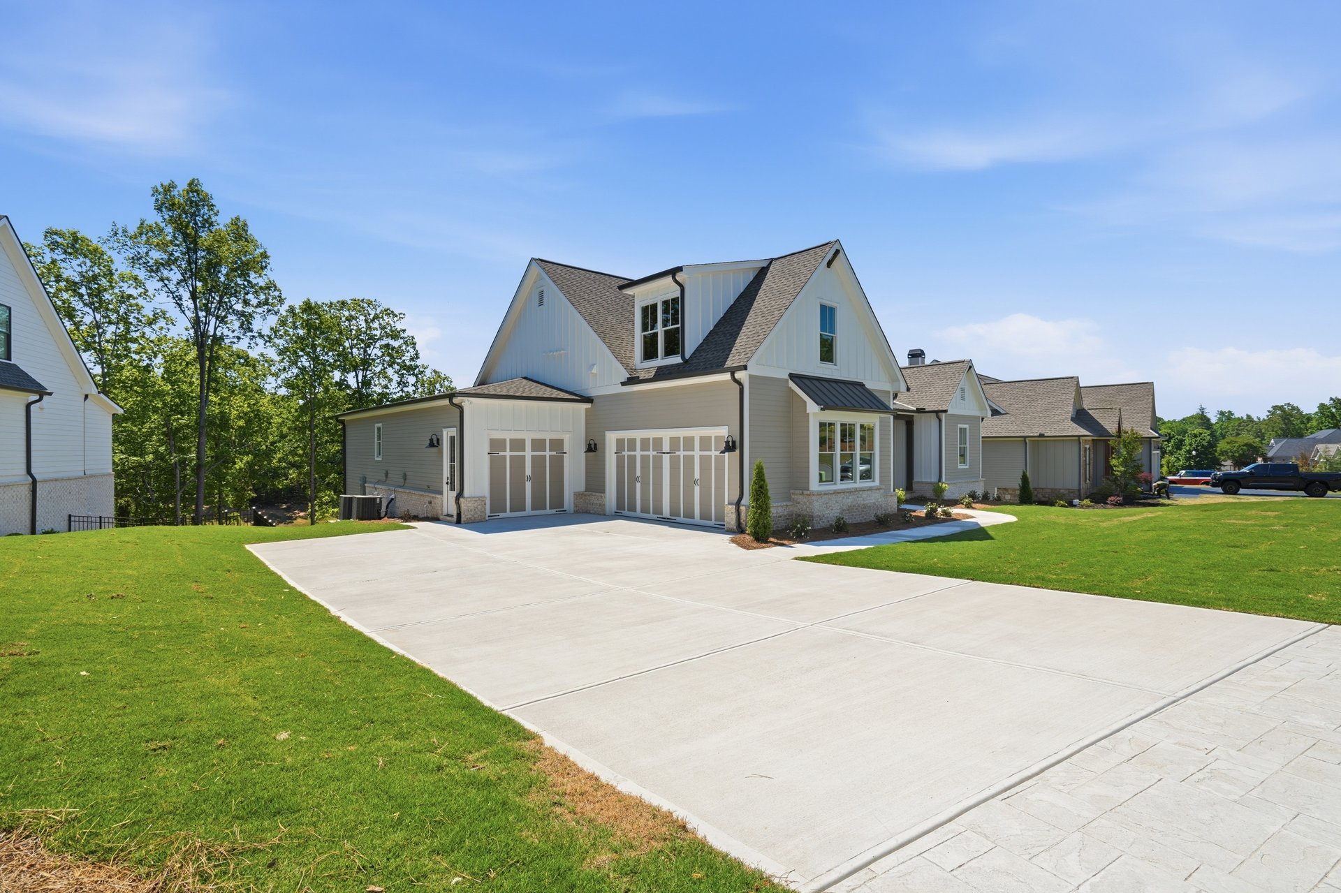 A modern house with a two-car garage, white siding, and a concrete driveway in a suburban neighborhood on a sunny day.
