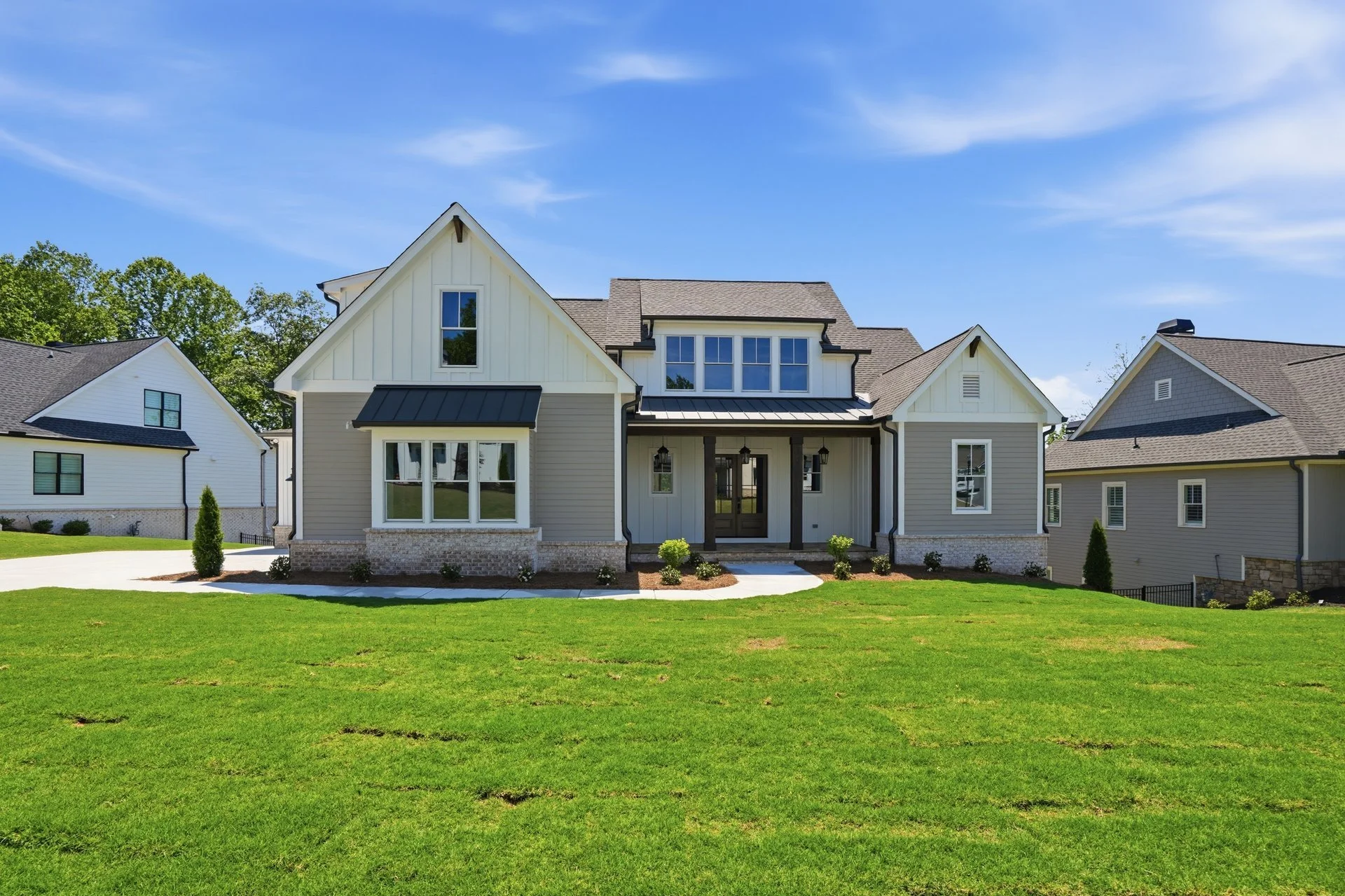 Front view of a modern house with a well-kept lawn, large windows, and a covered porch, under a bright blue sky.