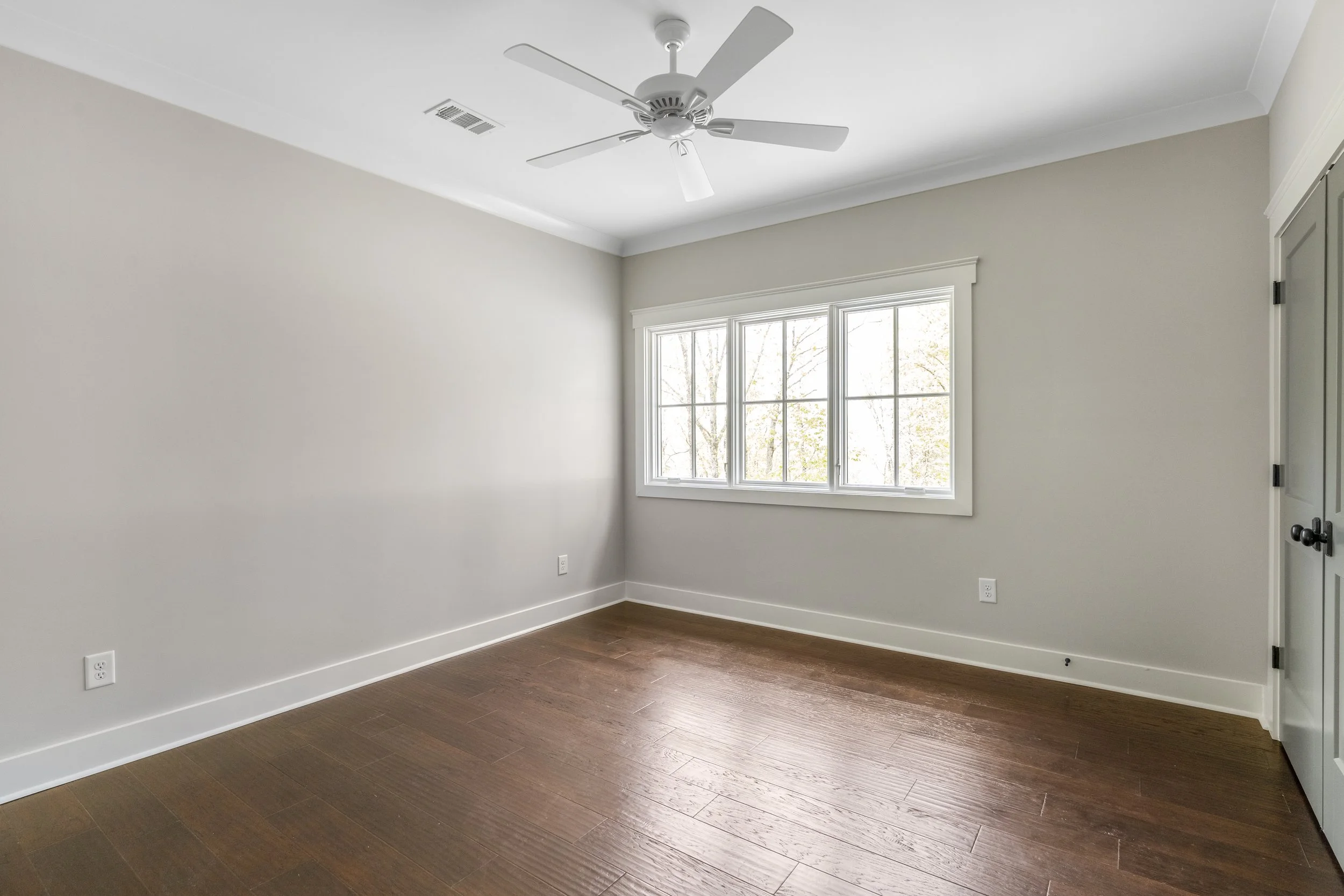 Empty room with white walls, hardwood flooring, a large window, and a ceiling fan.