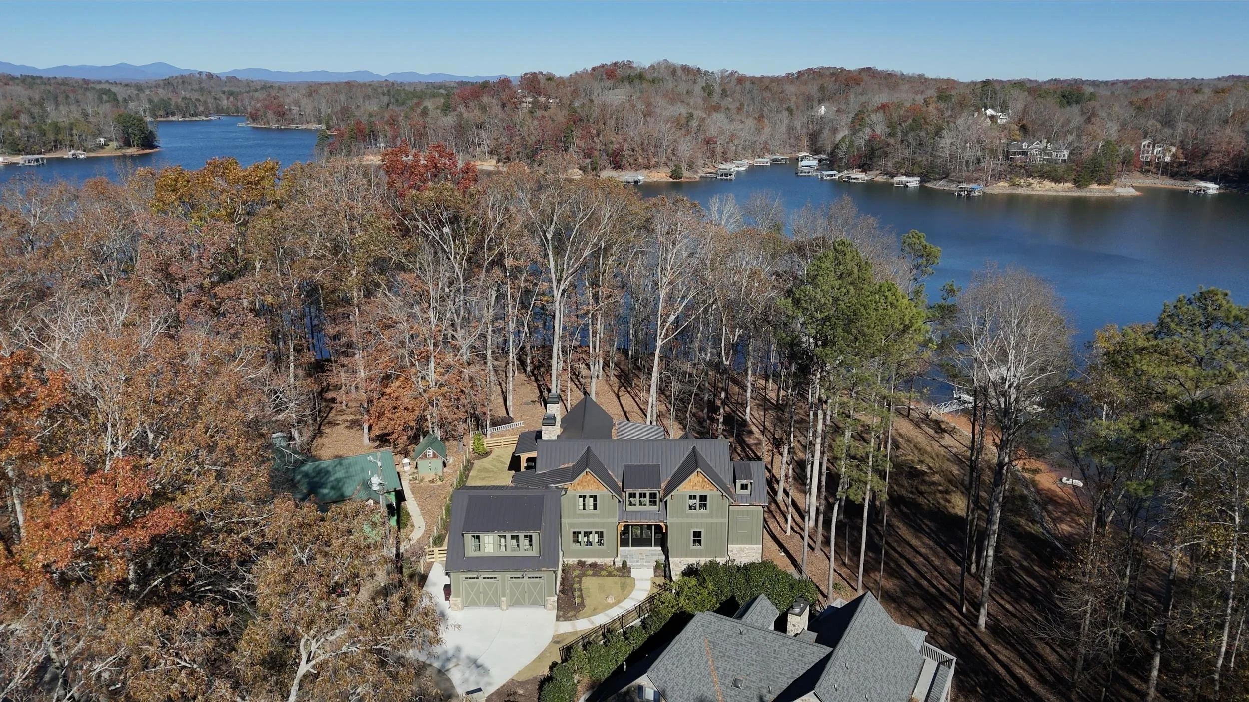Aerial view of a lakeside neighborhood during fall, with trees in autumn colors, a body of water with boats, and houses surrounded by trees.