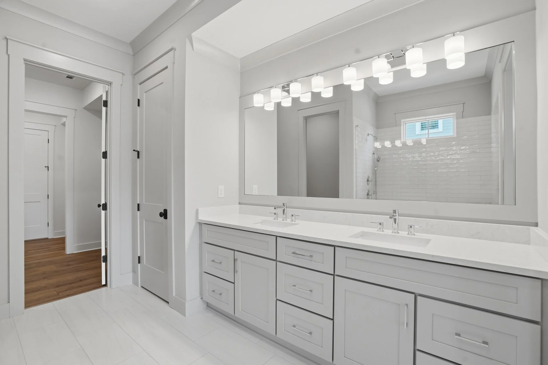 Modern white bathroom with large mirror, four light fixtures above, and a vanity with double sinks.