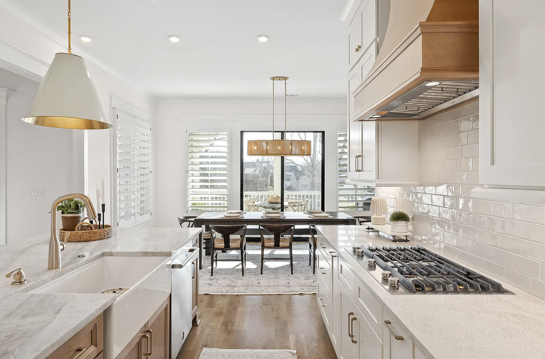 Bright, modern kitchen with white and wood cabinetry, a marble island, a gas cooktop, and a dining area with a wooden table and chairs near large windows and a sliding door.