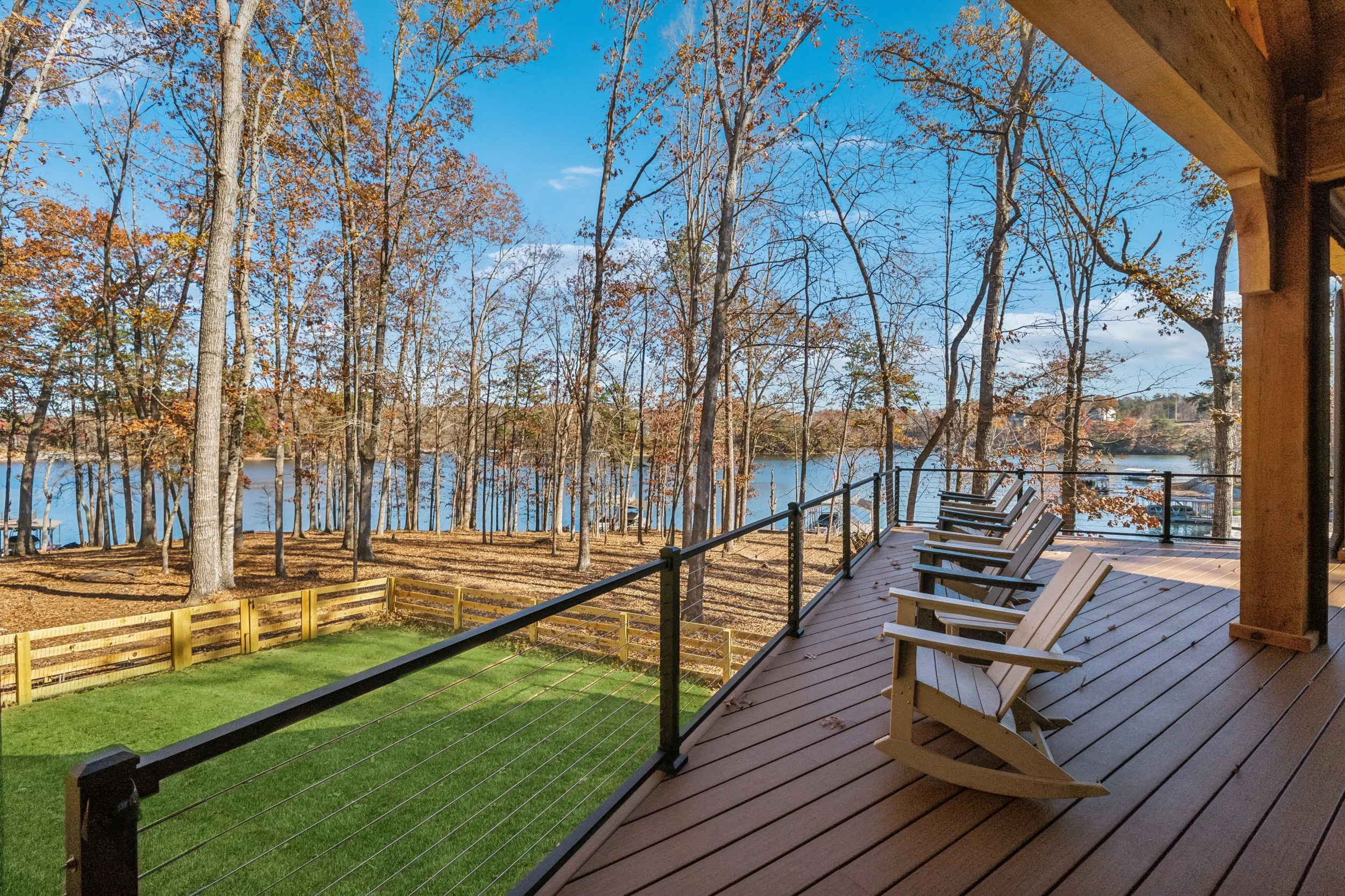 A view from a covered porch with Adirondack chairs overlooking a lake surrounded by trees with fall foliage, under a blue sky.