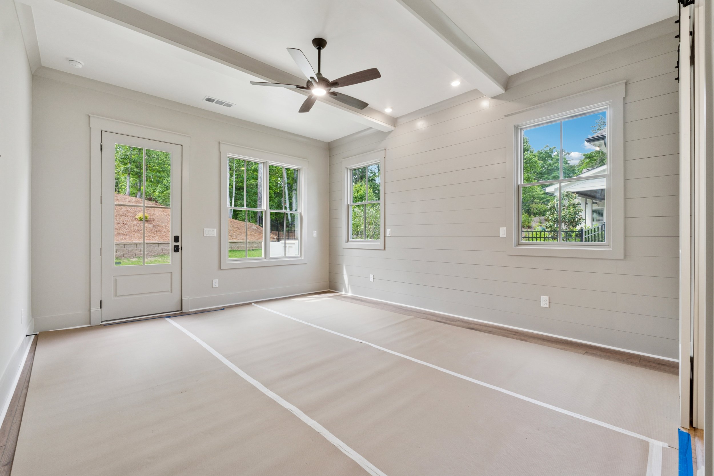 Empty room with large windows, white walls, ceiling fan, and natural light.