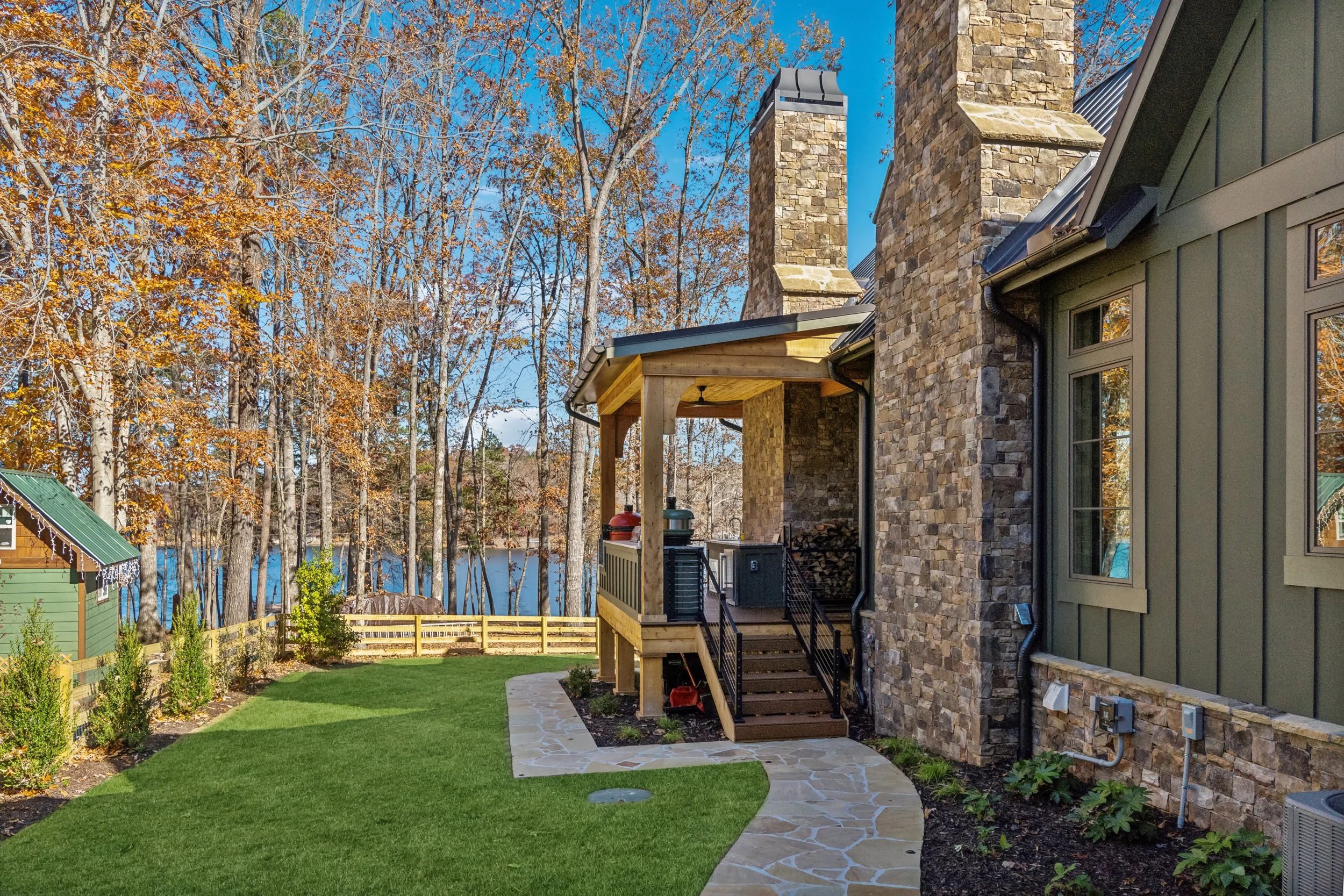 Backyard with stone and siding house, fire pit, green lawn, and trees with autumn leaves.