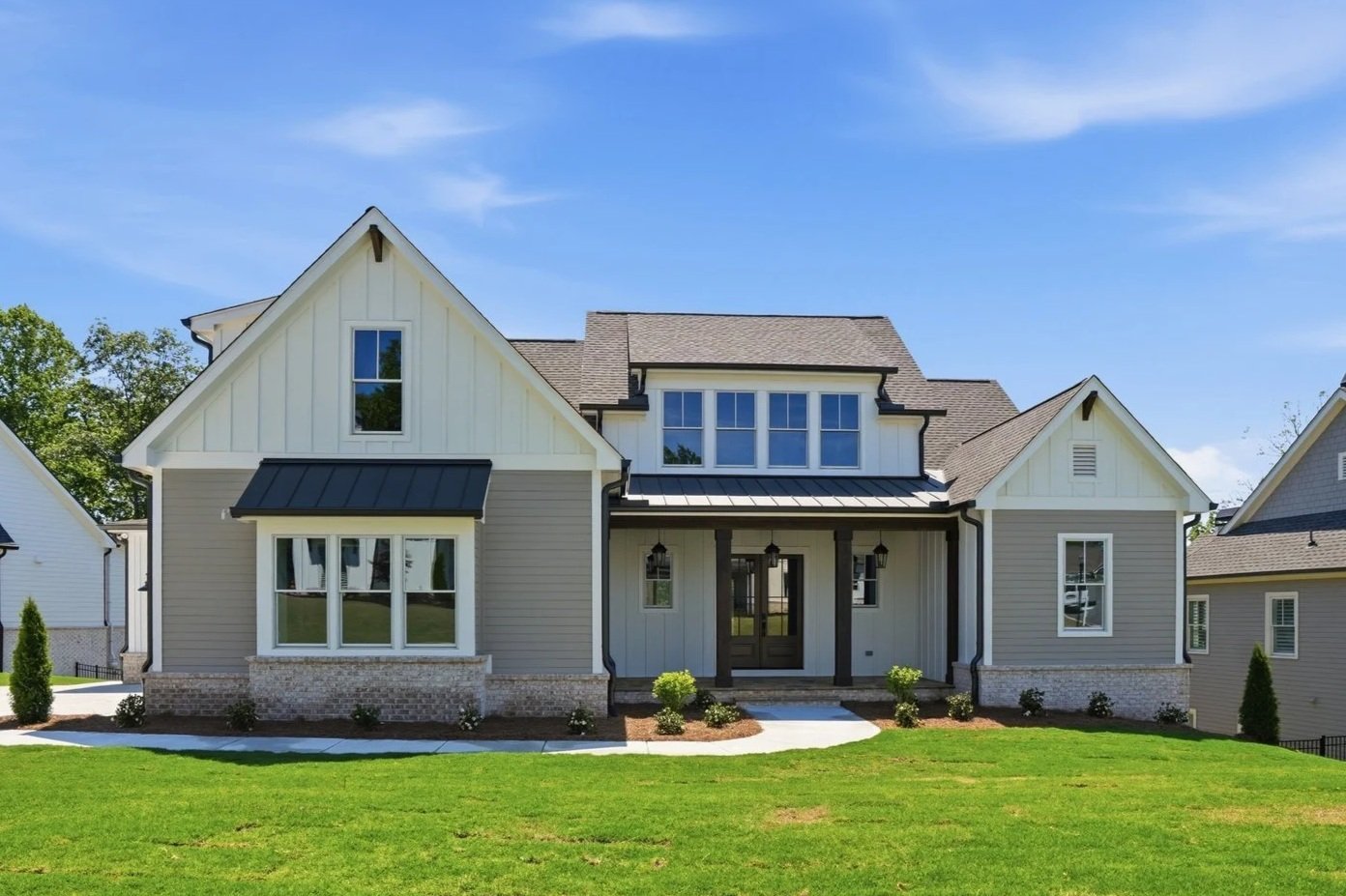 Front view of a modern two-story suburban house with gray siding, black roof, large windows, and a green lawn in front.
