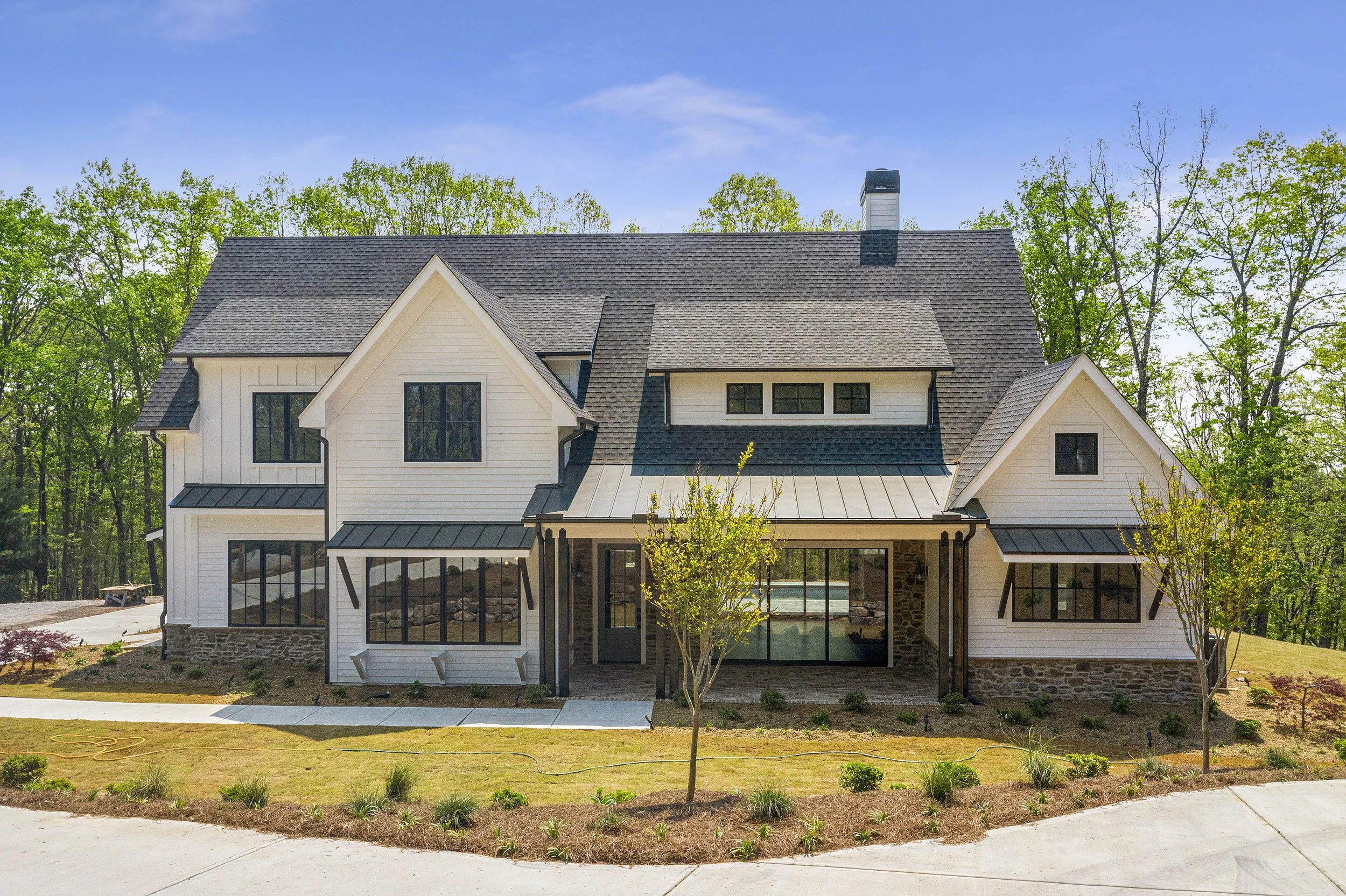 A modern house with a white exterior, large windows, and a shingled roof, surrounded by trees and a landscaped yard.