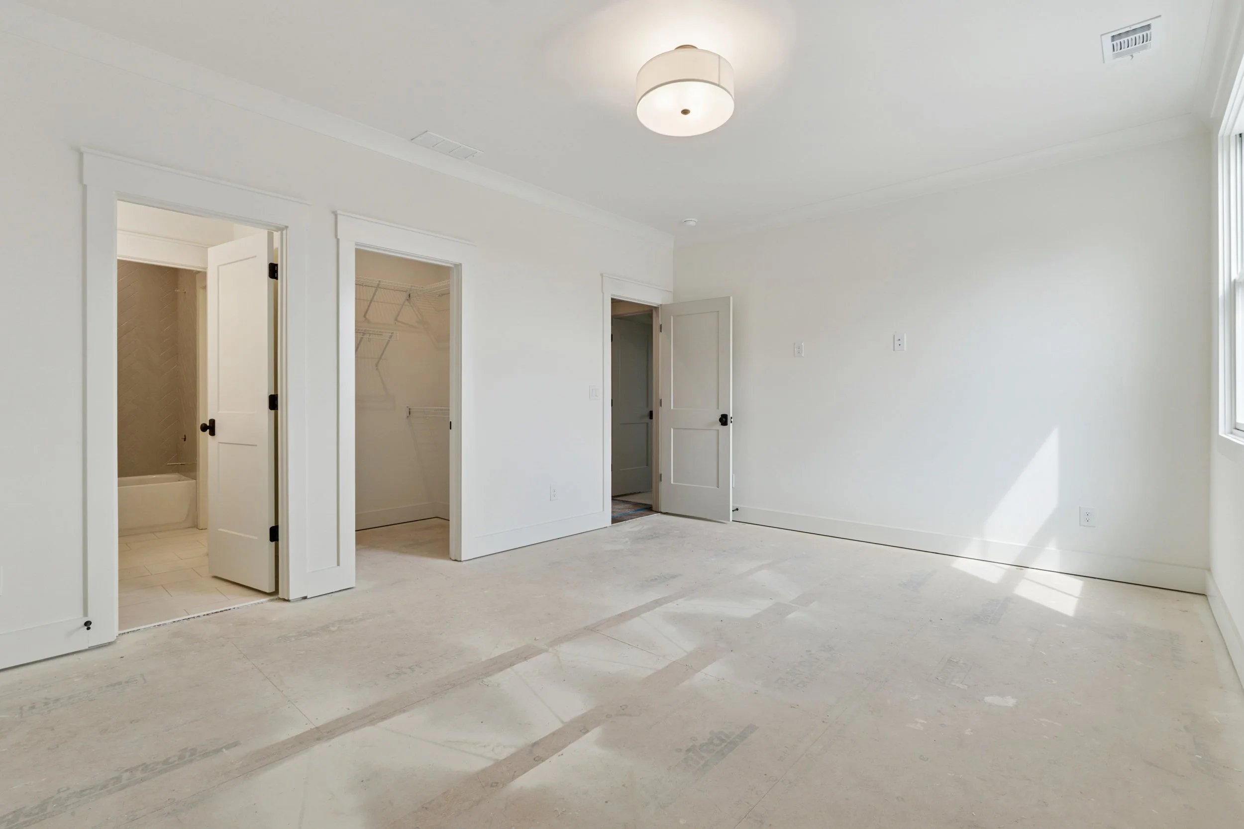 Empty room with white walls, windows, open closet, and bathroom door.