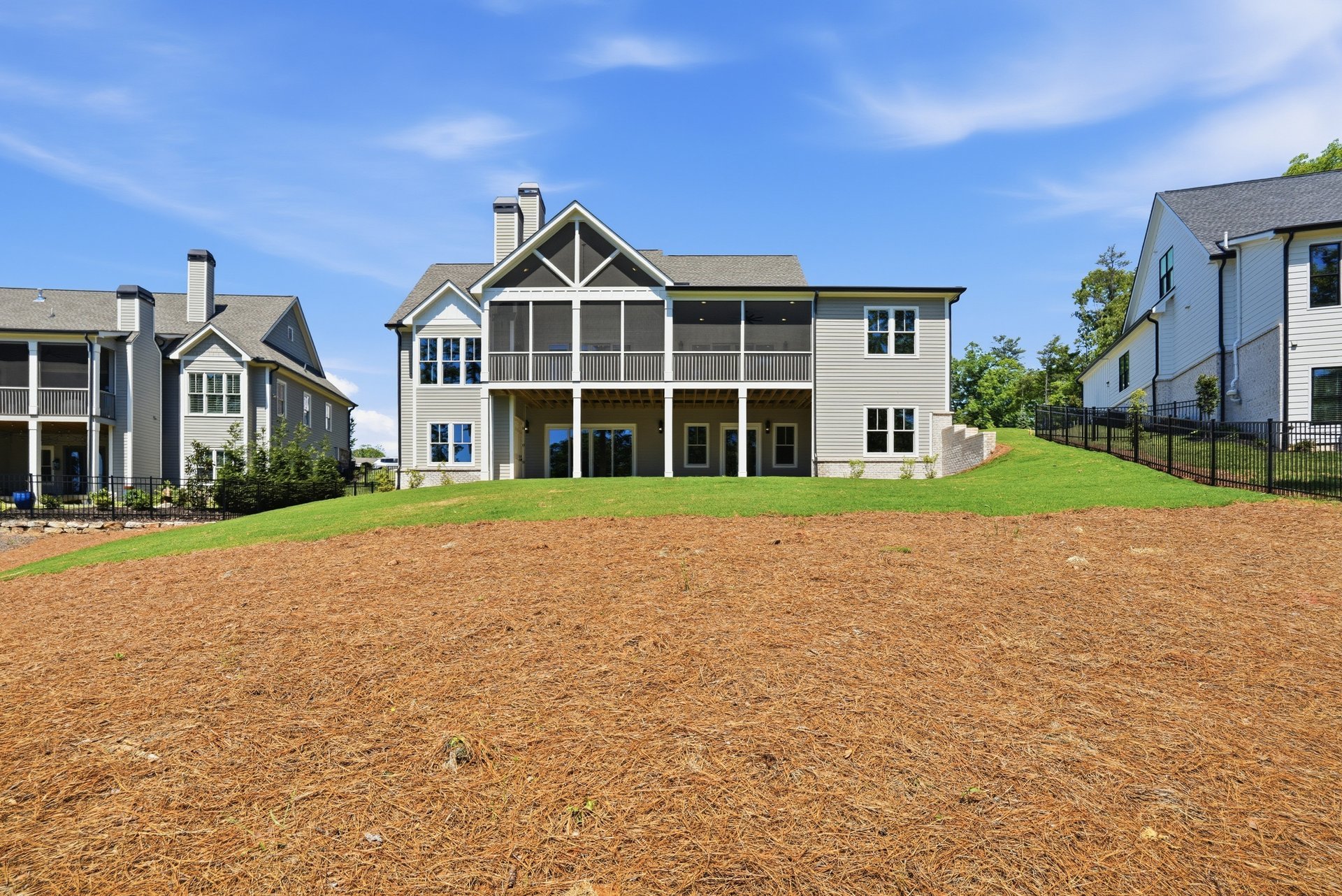Multiple modern houses with white siding, black shutters, and screened porches, surrounded by well-maintained lawns and fences, under a bright blue sky.