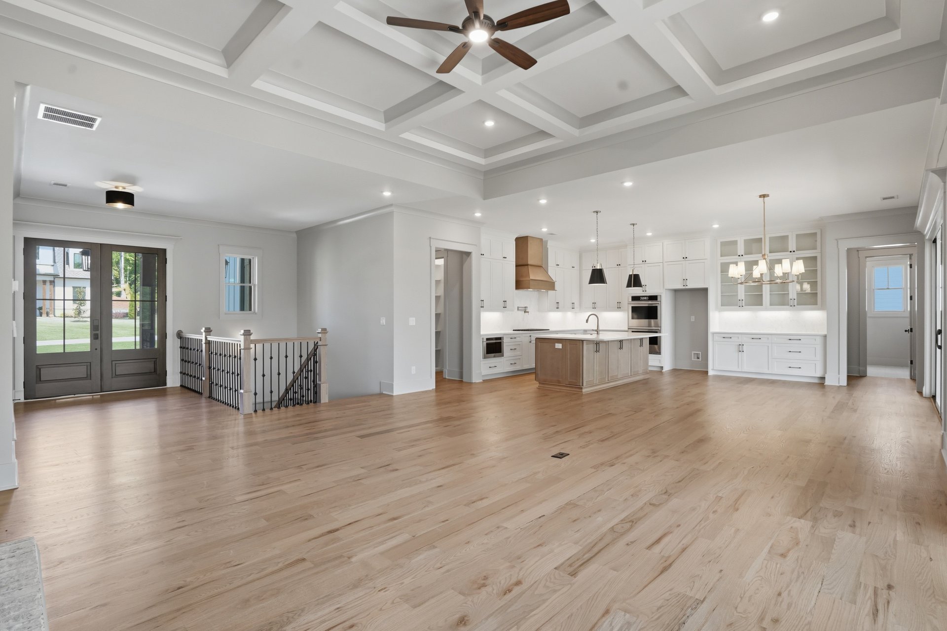 Open-concept living space with hardwood floors, white kitchen cabinets, center island, and multiple light fixtures, including a ceiling fan.
