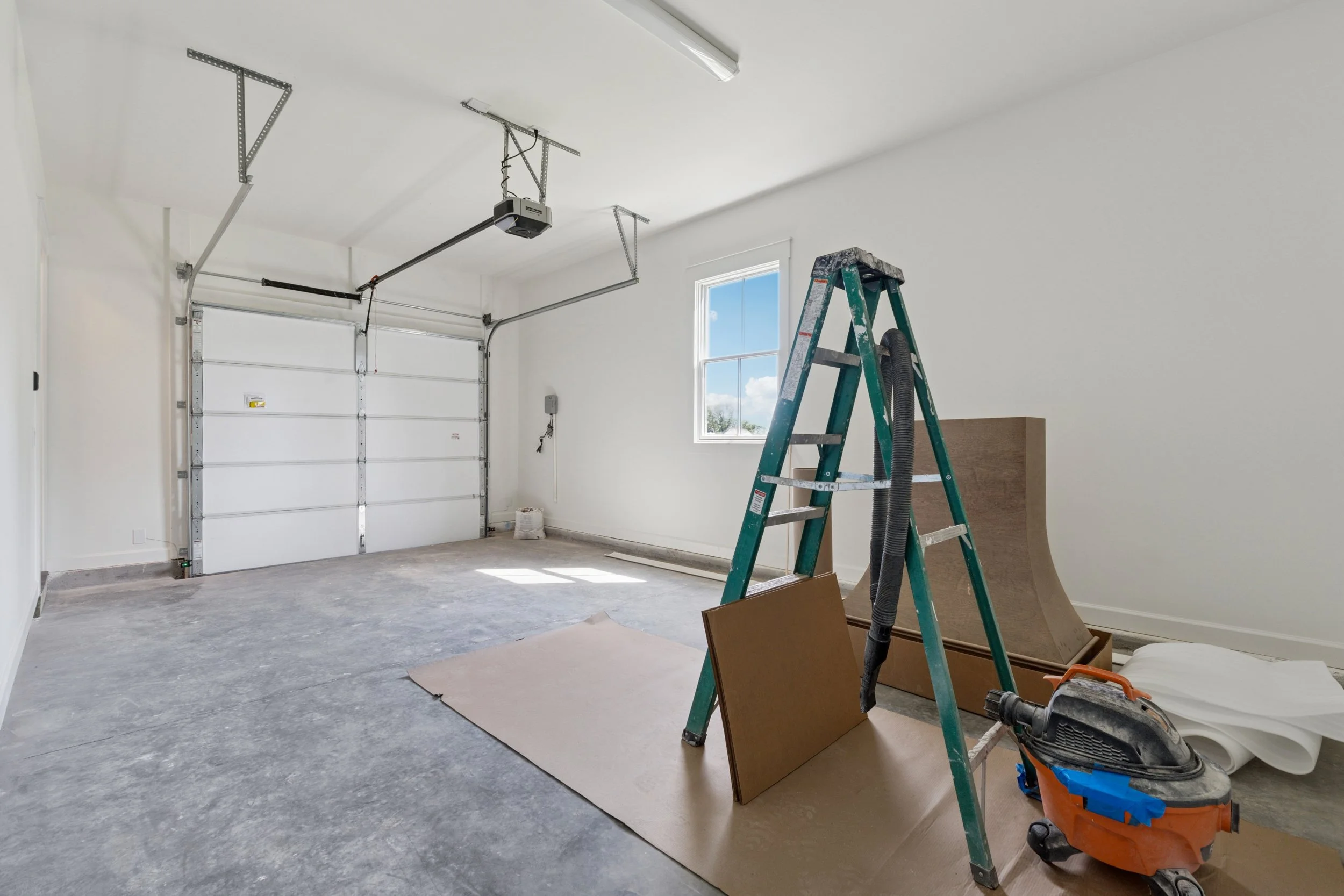 Empty garage with a ladder, construction tools, and materials, ready for renovation or painting.