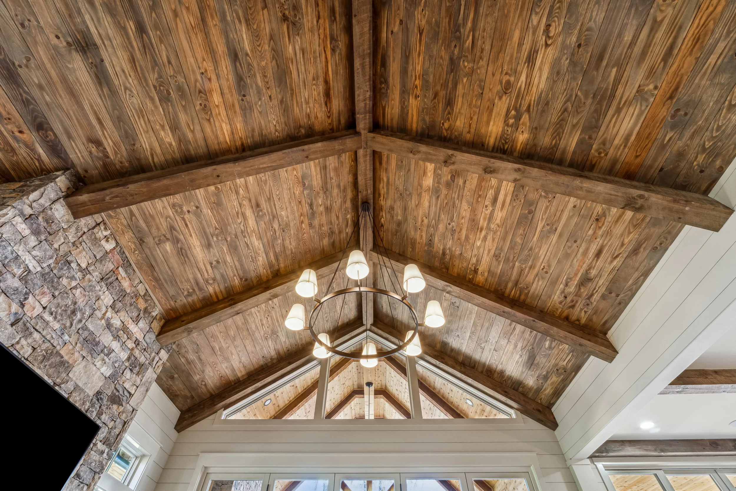 Wooden ceiling with exposed beams and a chandelier light fixture in a spacious room.
