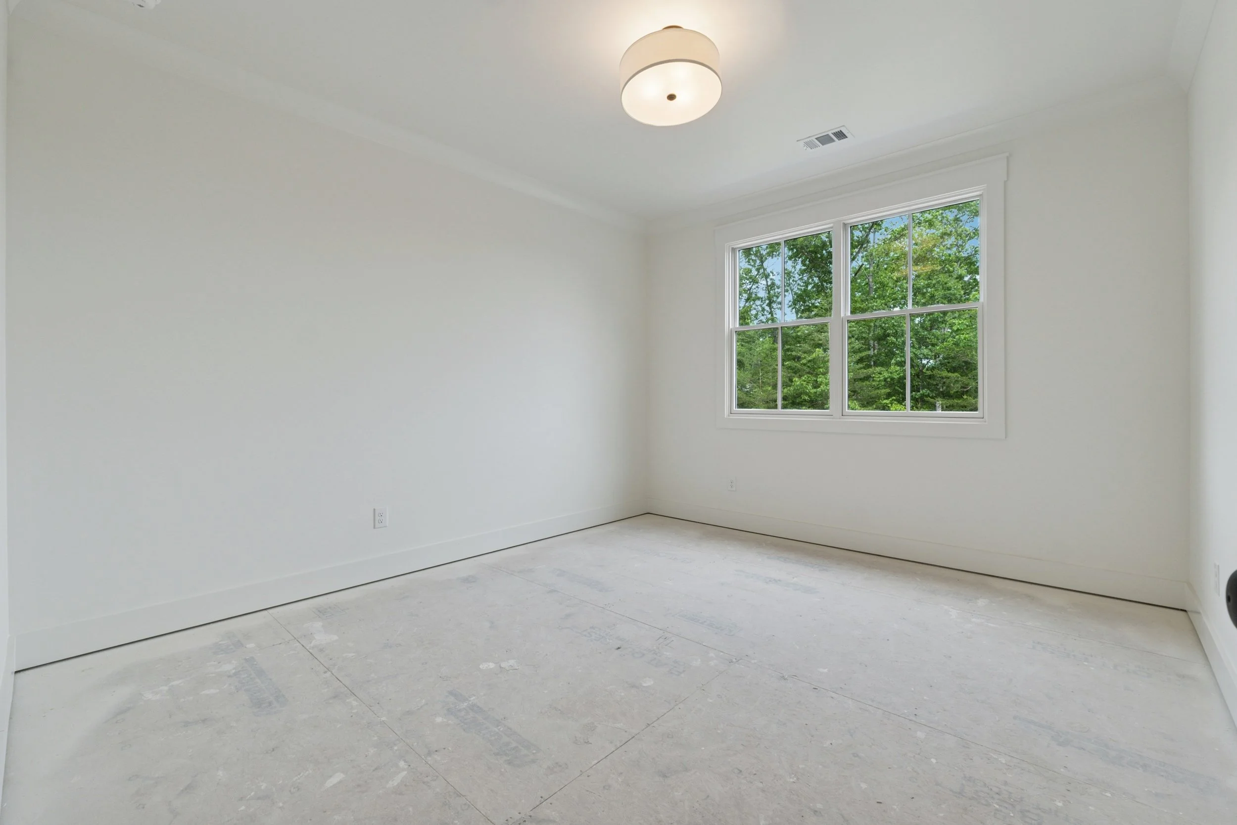 Empty room with white walls, a window with green trees outside, and a ceiling light fixture.