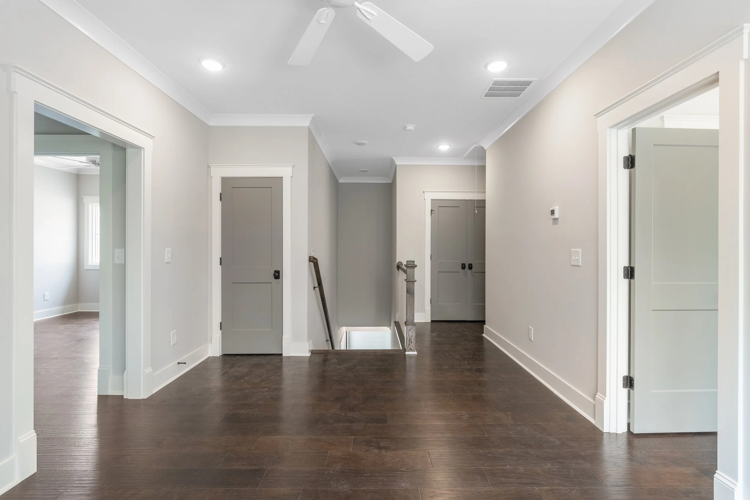 Interior hallway with white walls, dark hardwood flooring, multiple doorways, and ceiling lights.