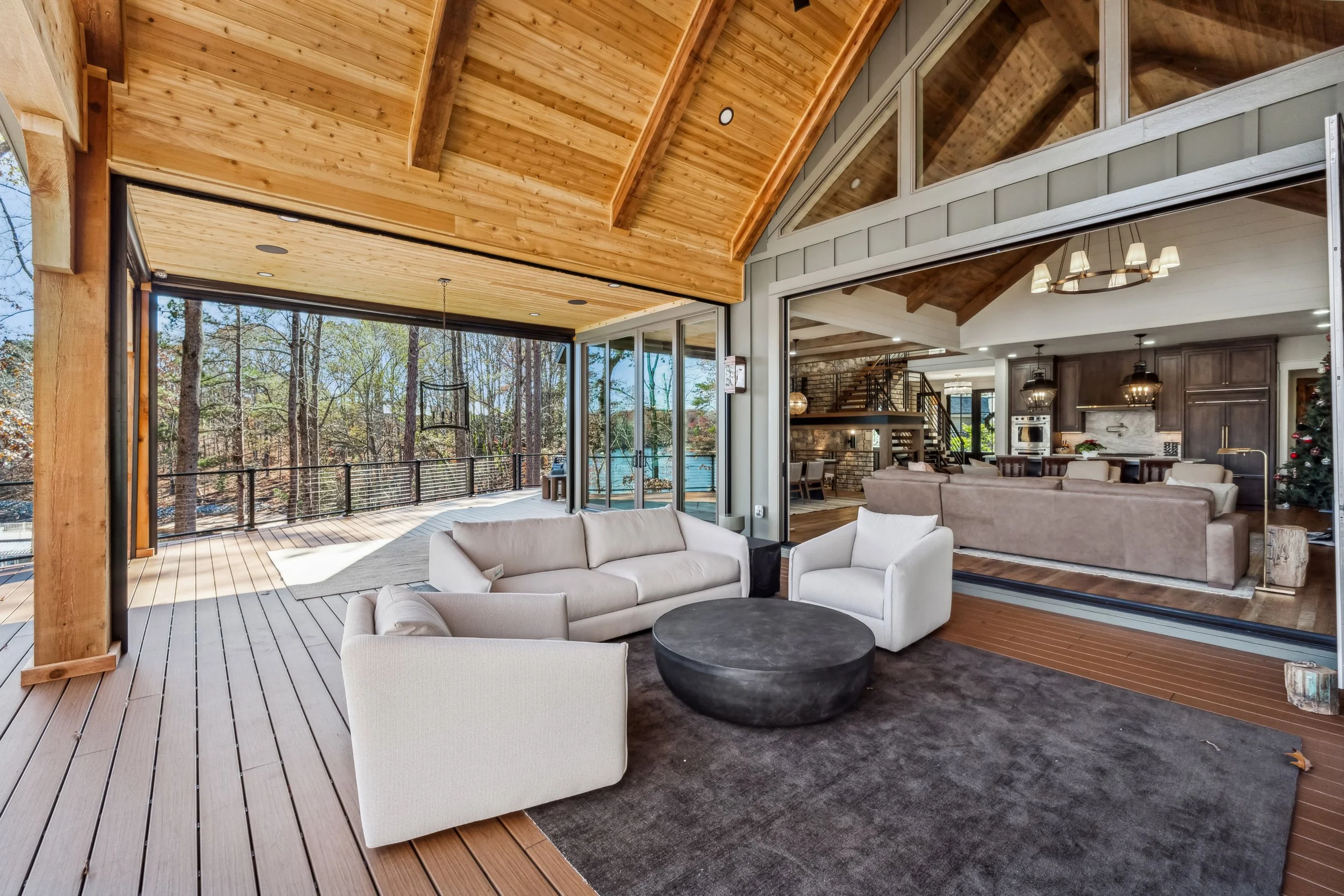 Living room with large windows, beige furniture, and a view of a wooded outdoor deck area.